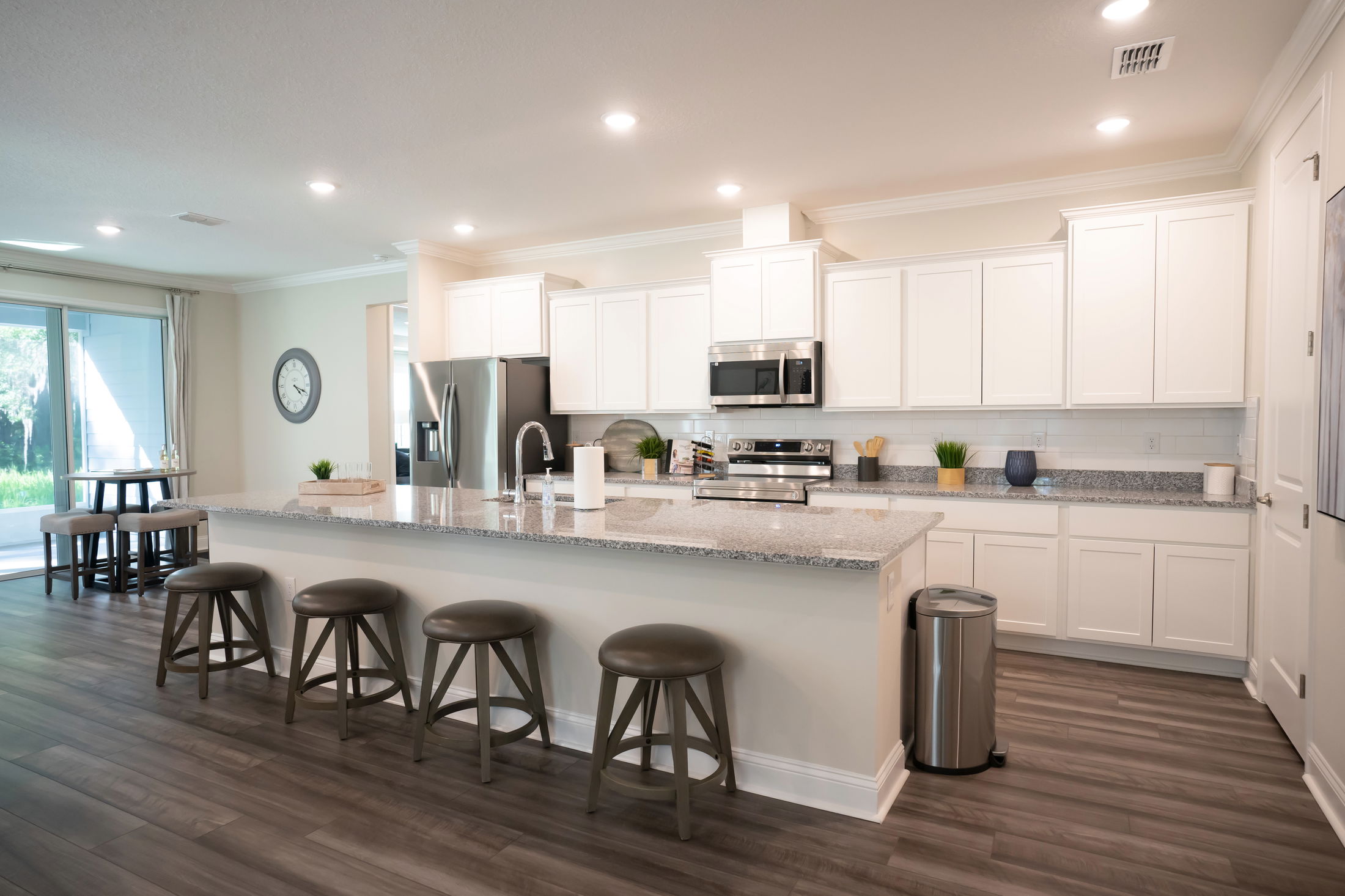 Modern kitchen with white cabinets, stainless steel appliances, and a large granite island with bar stools.