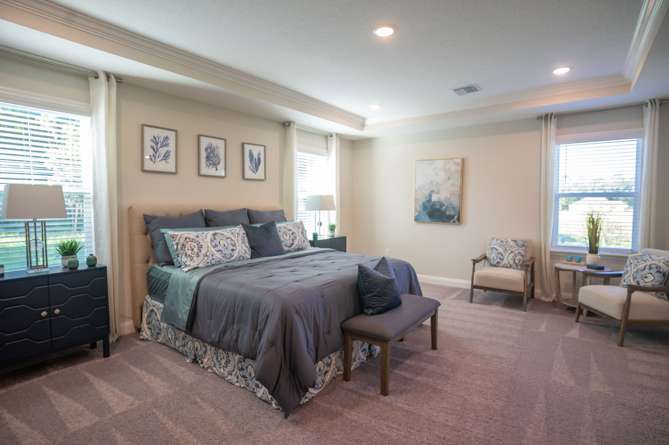 Elegant modern bedroom with a large bed, blue-gray bedding, wall art, and abundant natural light.
