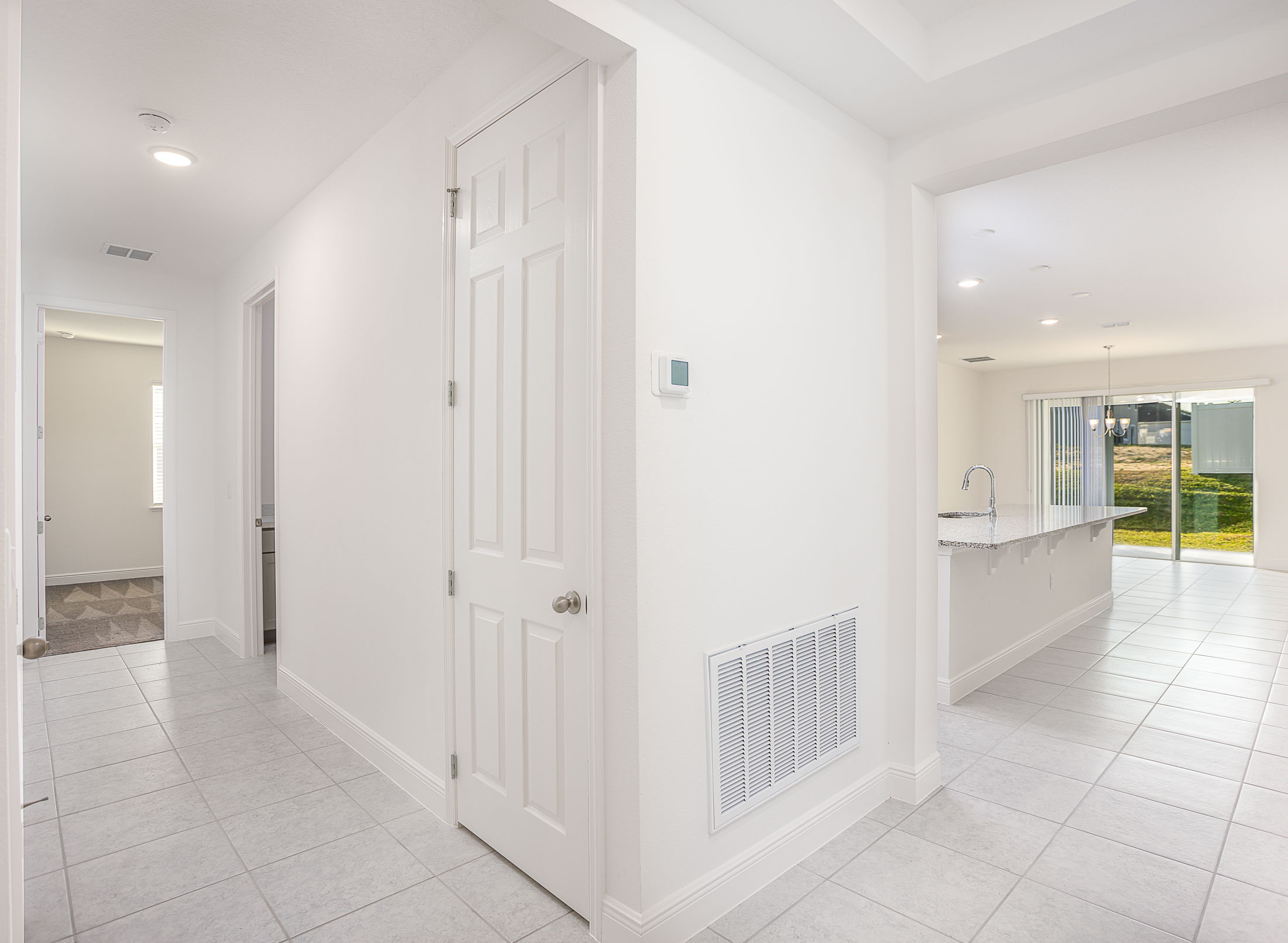Modern hallway with white walls leading to an open kitchen area with large windows and natural lighting.