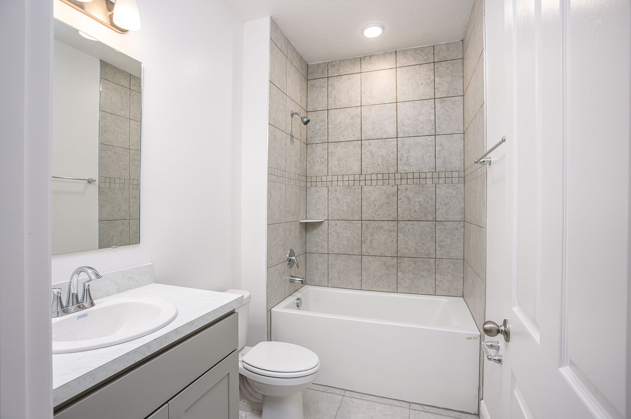 Modern white bathroom featuring a tiled shower-bathtub combination, marble countertop, and sleek fixtures.
