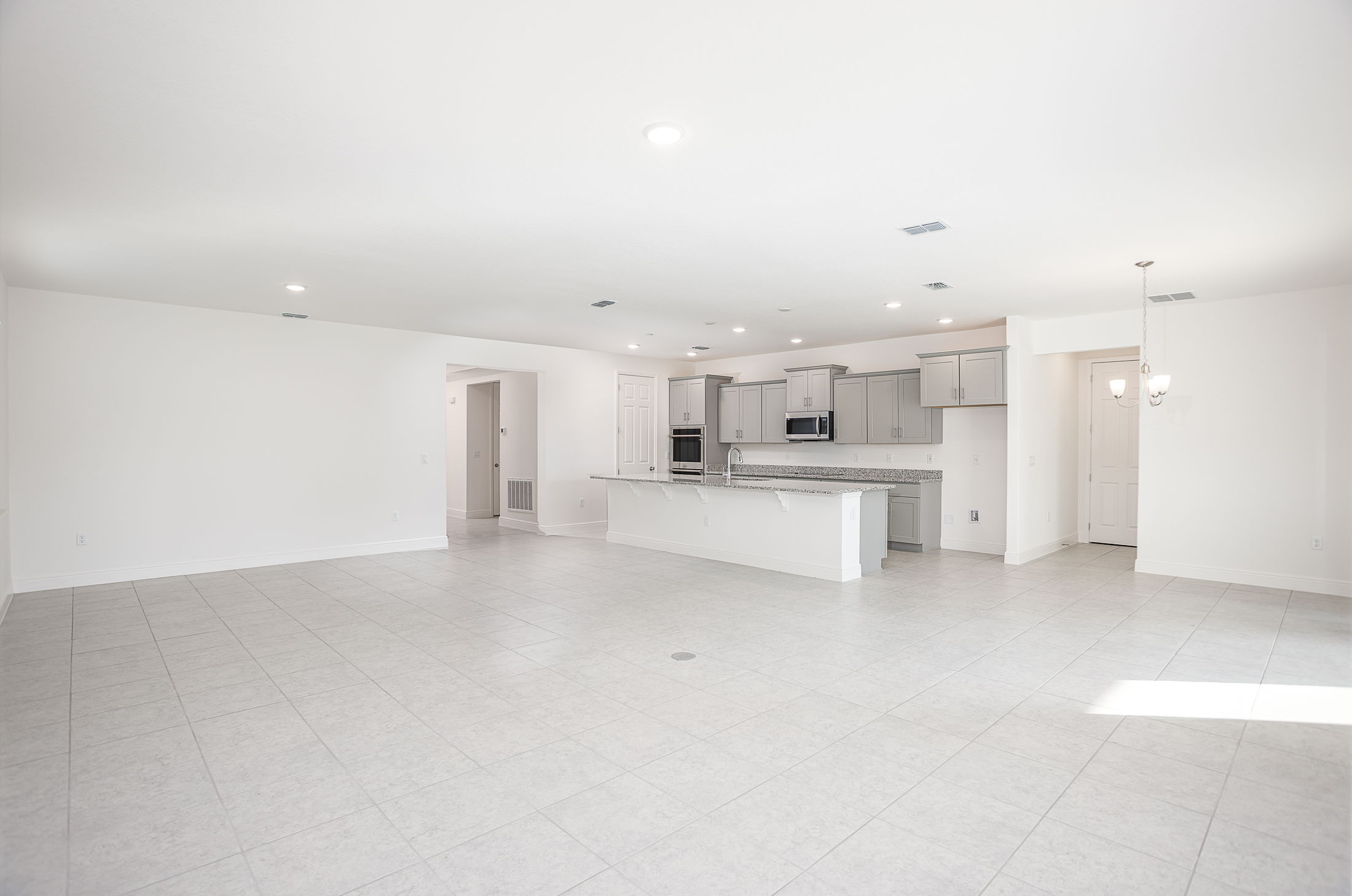 Spacious open-concept kitchen and living area with modern gray cabinets, granite countertops, and tile flooring in a bright, empty room.