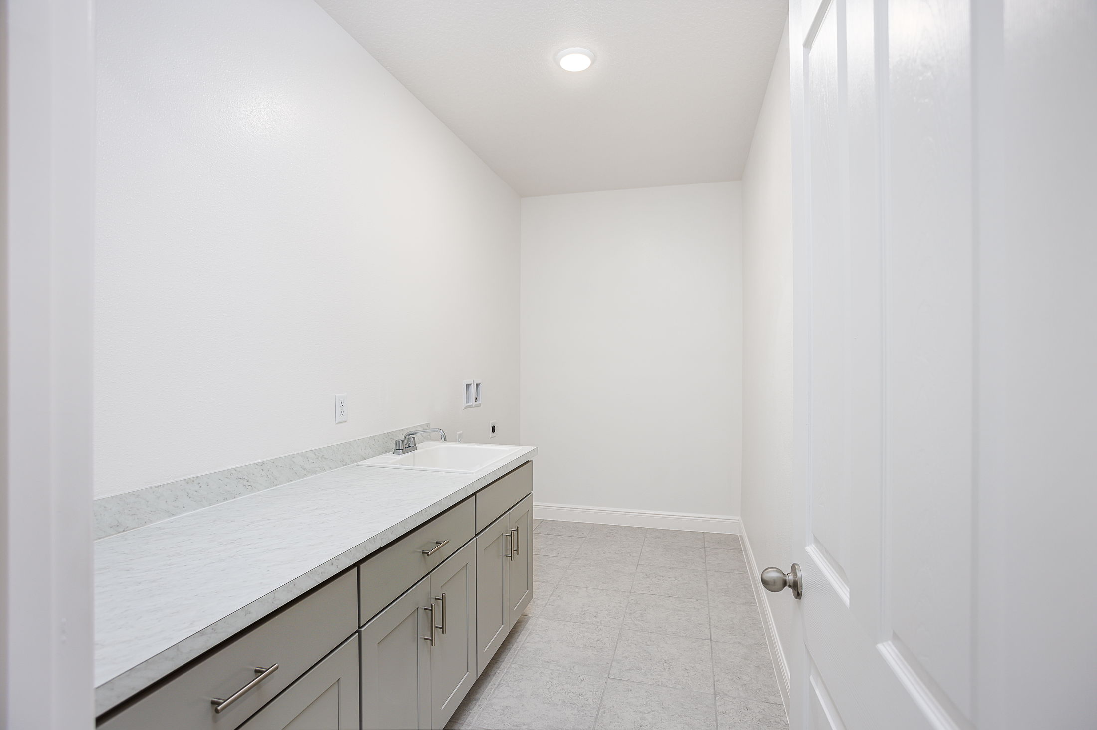 Image of a modern, minimalistic laundry room with light gray cabinetry, marble countertop, and a stainless steel sink.