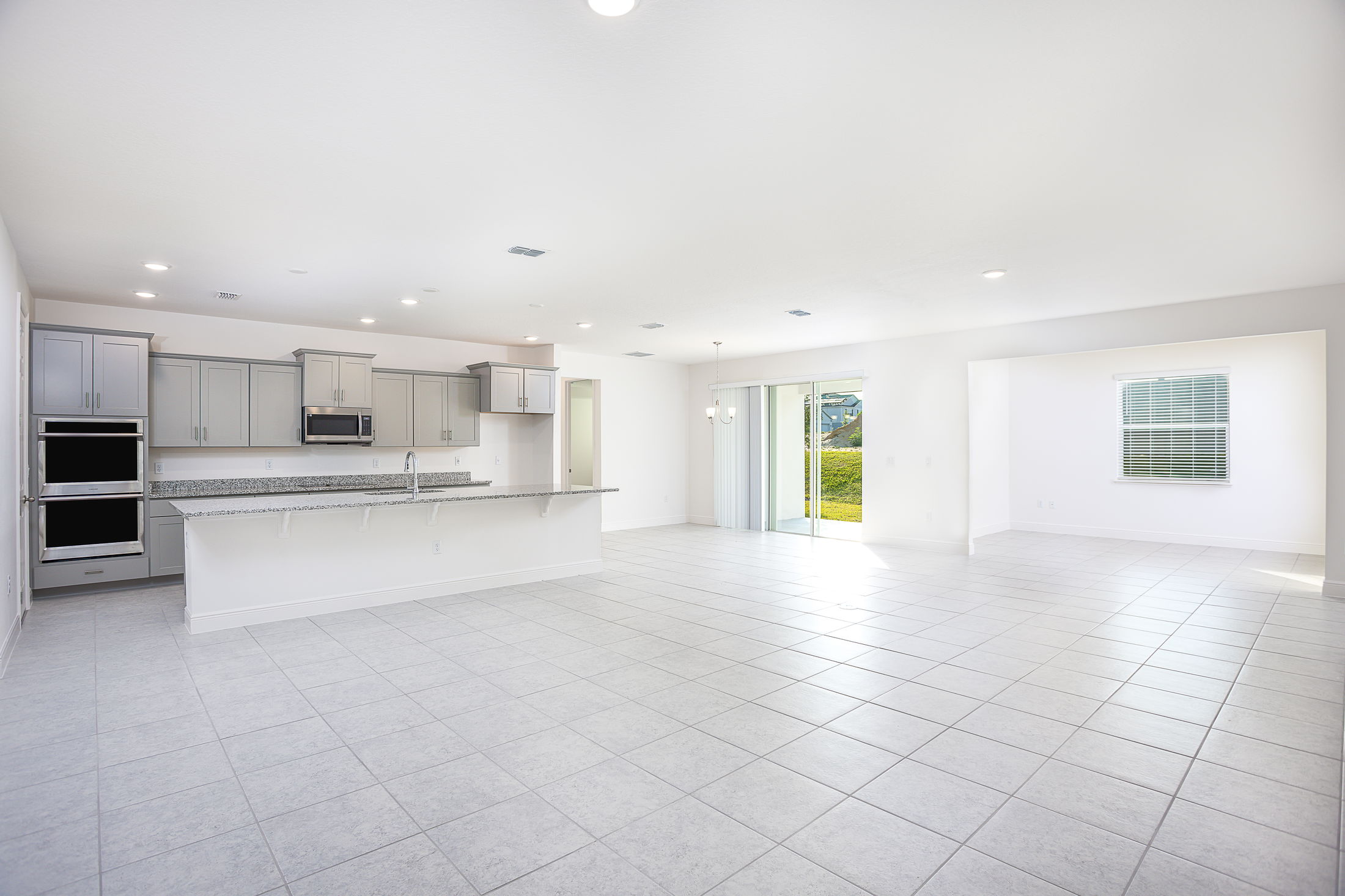 Spacious, modern open-concept kitchen and living area with gray cabinets, granite countertops, and natural light from sliding glass doors.