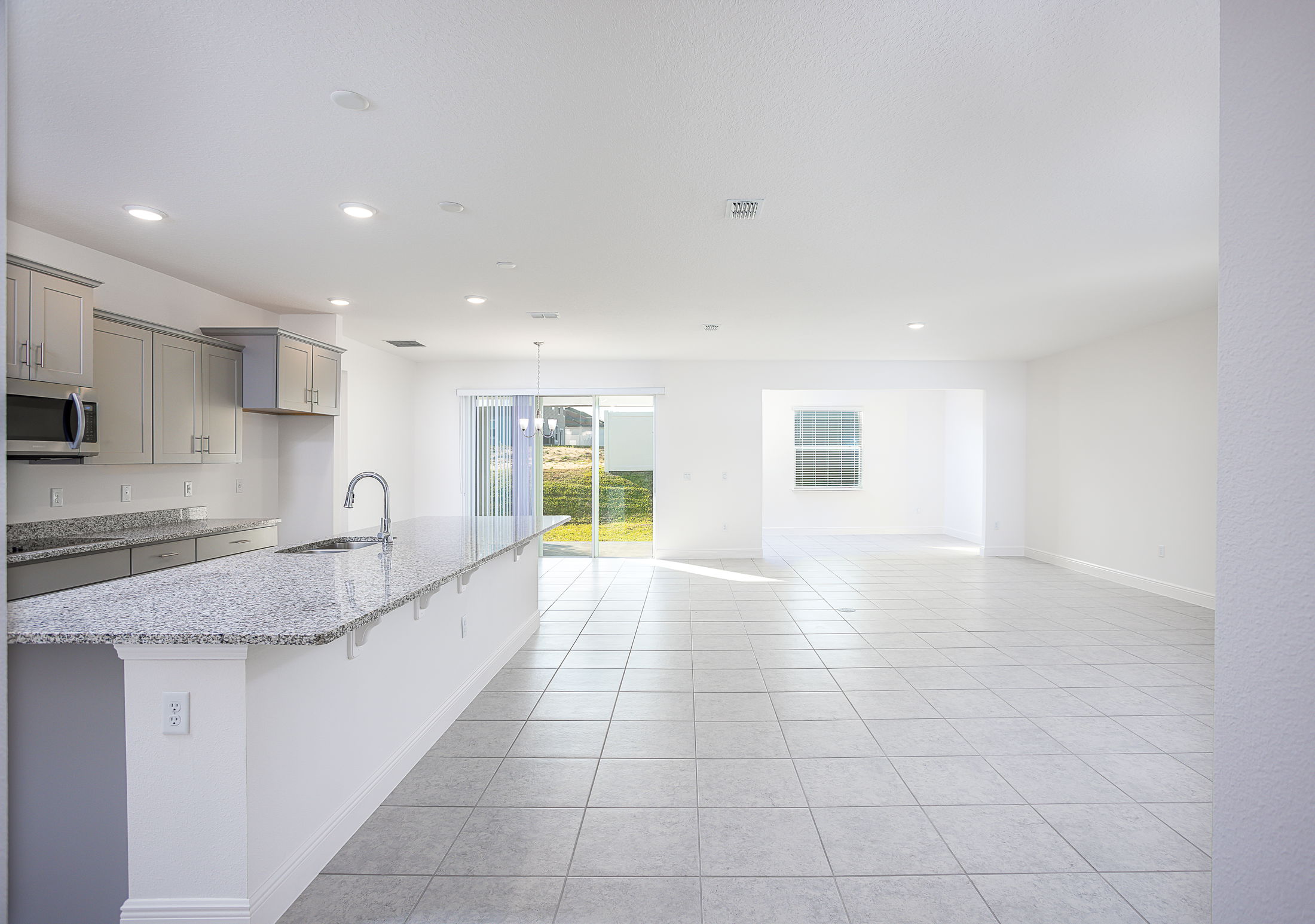 Spacious modern kitchen and living area with granite countertops, tile flooring, and sliding patio doors.