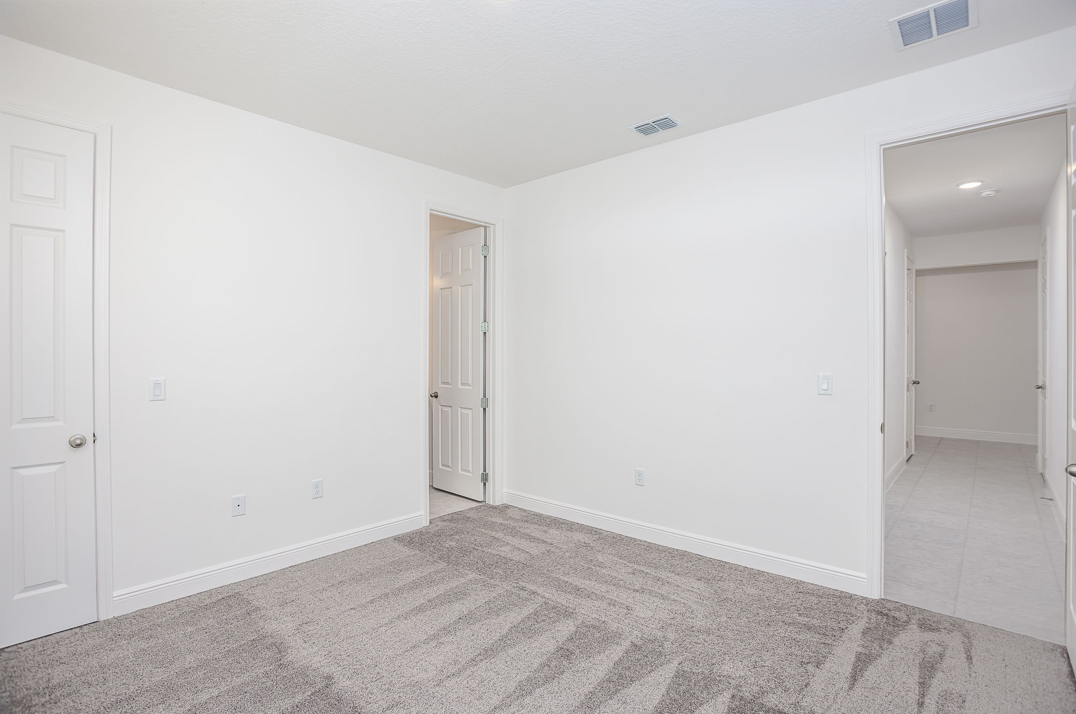 Empty white-walled room with gray carpet and multiple doors, showcasing a clean and modern interior.