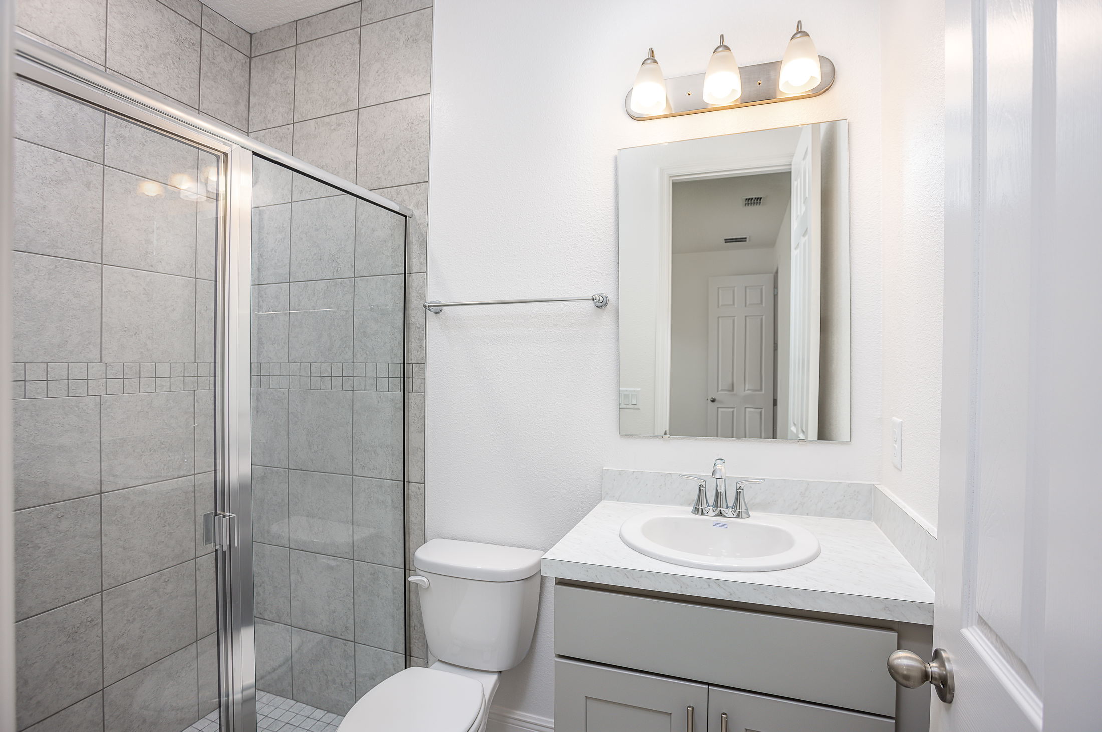Modern bathroom featuring a glass-enclosed shower, marble countertop sink, and bright lighting.