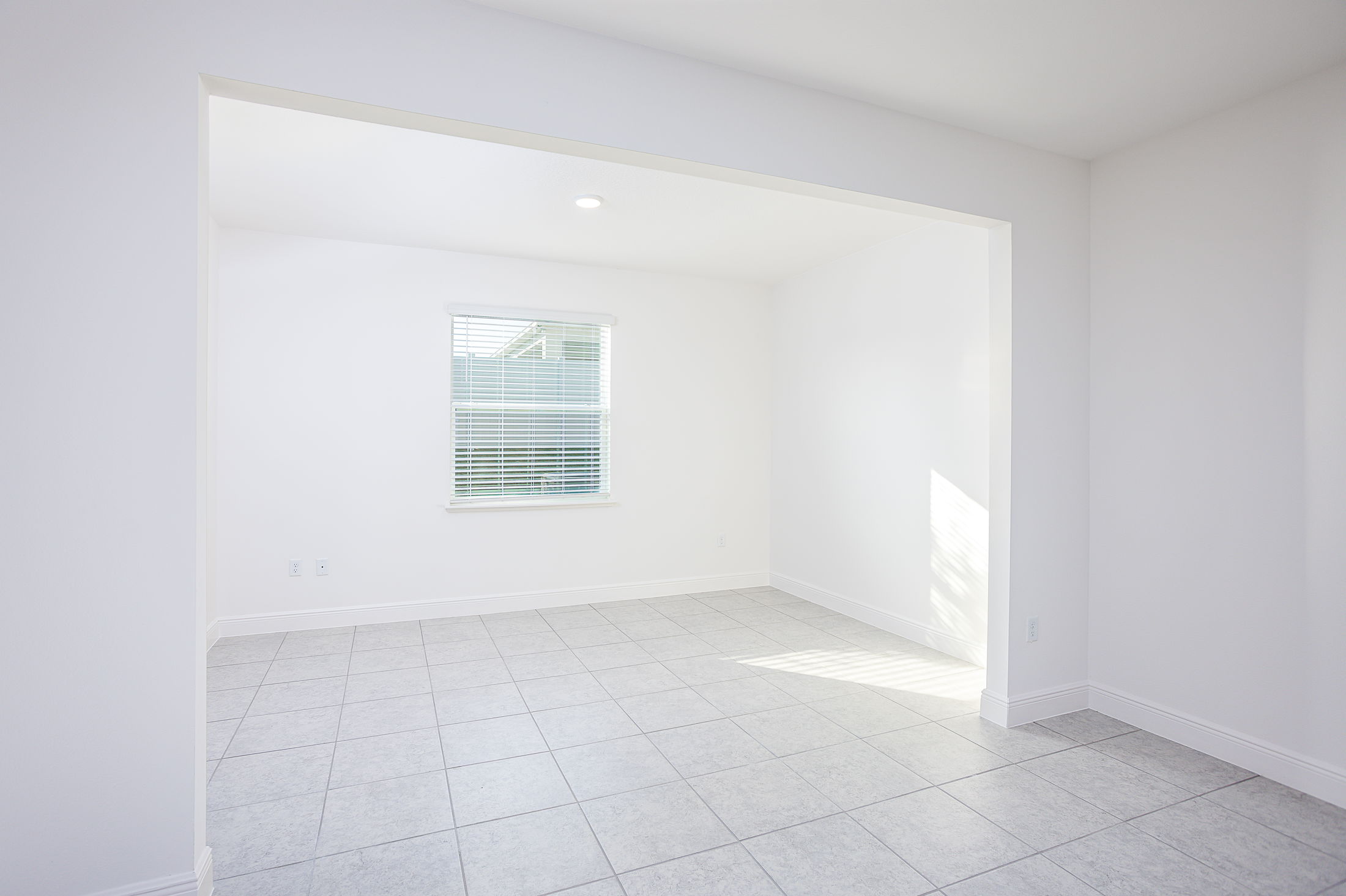 Bright, empty room with tiled floor, white walls, and a window with blinds.