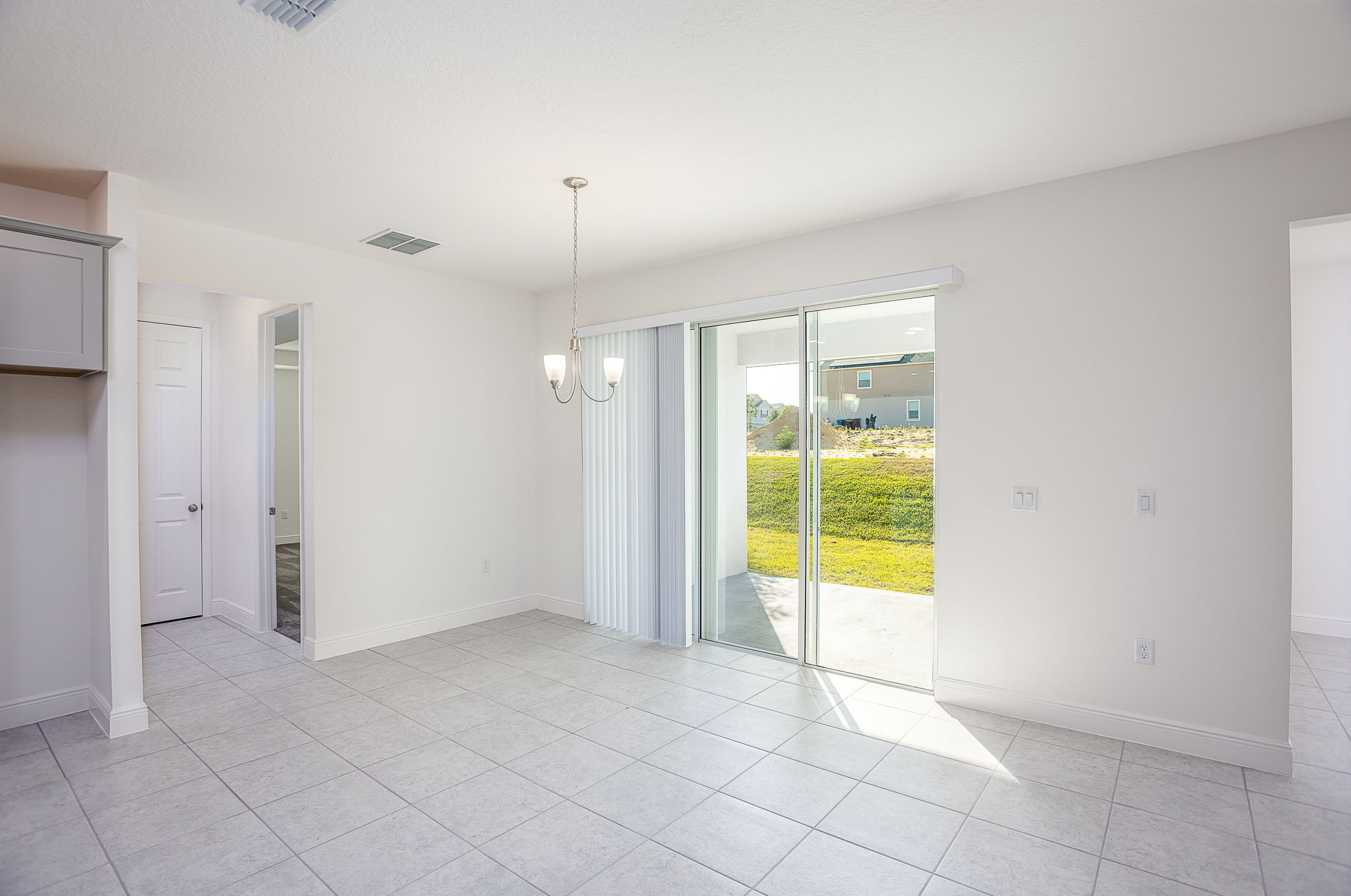 Modern, empty tiled room with sliding glass doors opening to a grassy backyard.