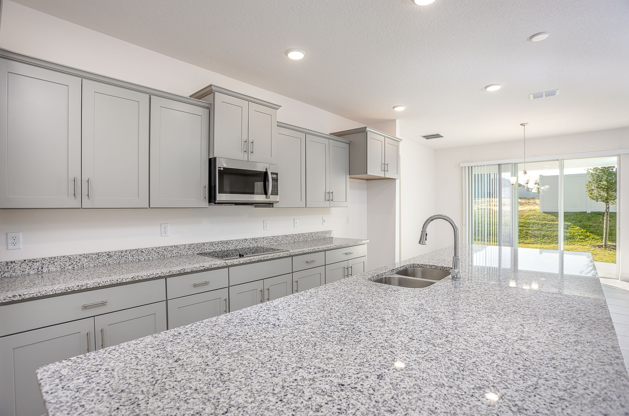 Modern kitchen with gray cabinets and granite countertops, featuring stainless steel appliances and a view of the backyard through sliding glass doors.