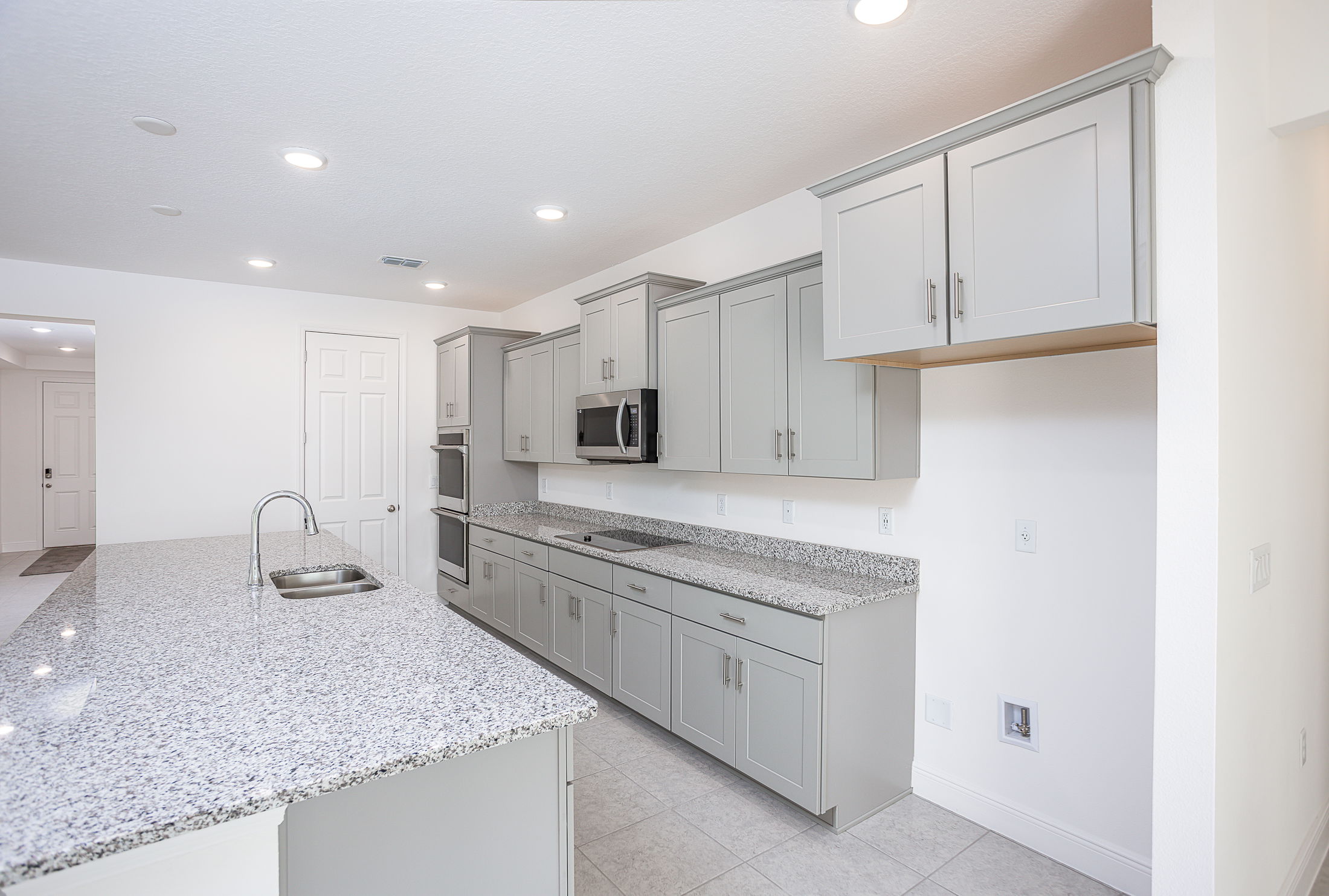 Modern kitchen with gray cabinets, granite countertops, and stainless steel appliances under recessed lighting.