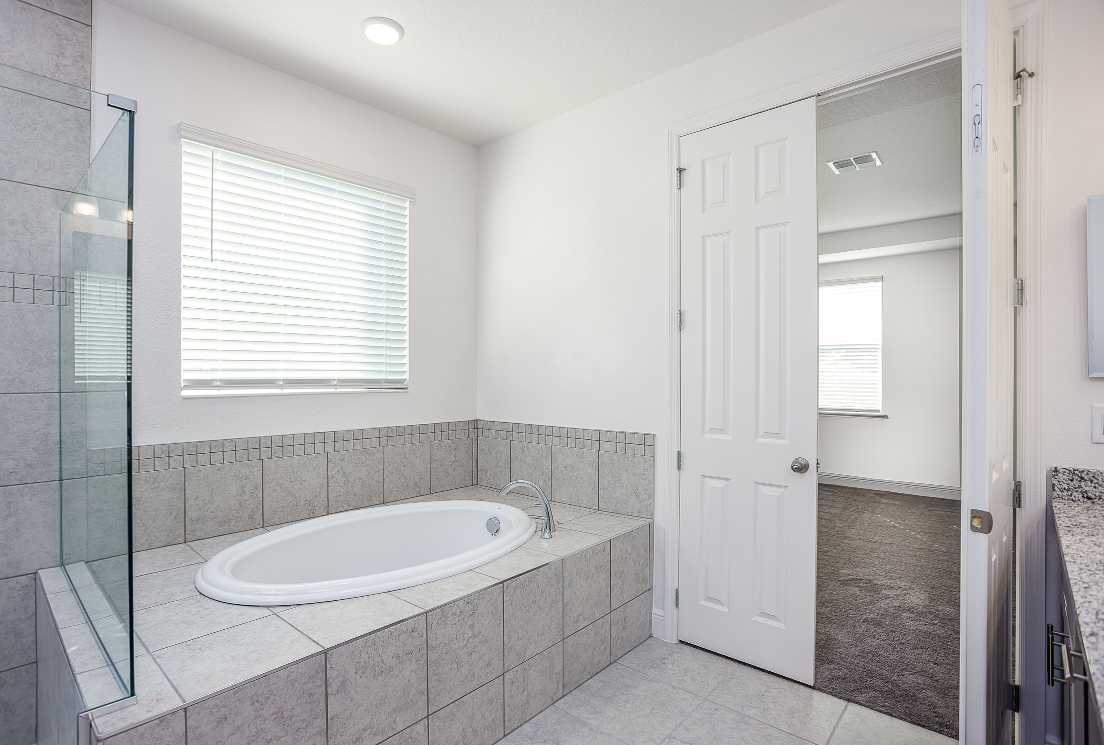 Modern bathroom with a built-in tiled bathtub, glass shower enclosure, and a white door leading to an adjoining room.