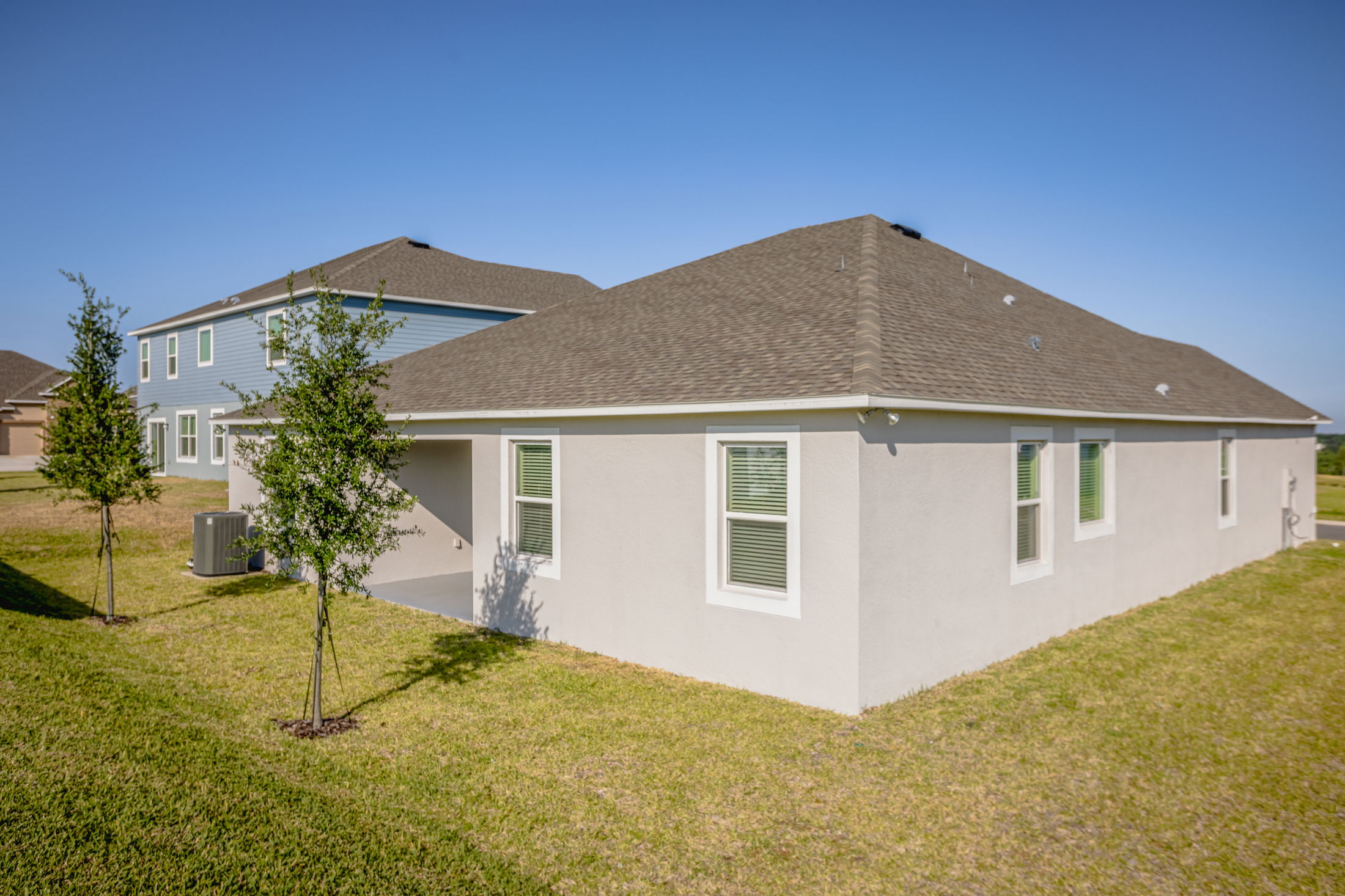 Modern suburban home with a light-colored exterior and neatly landscaped yard under a clear blue sky.