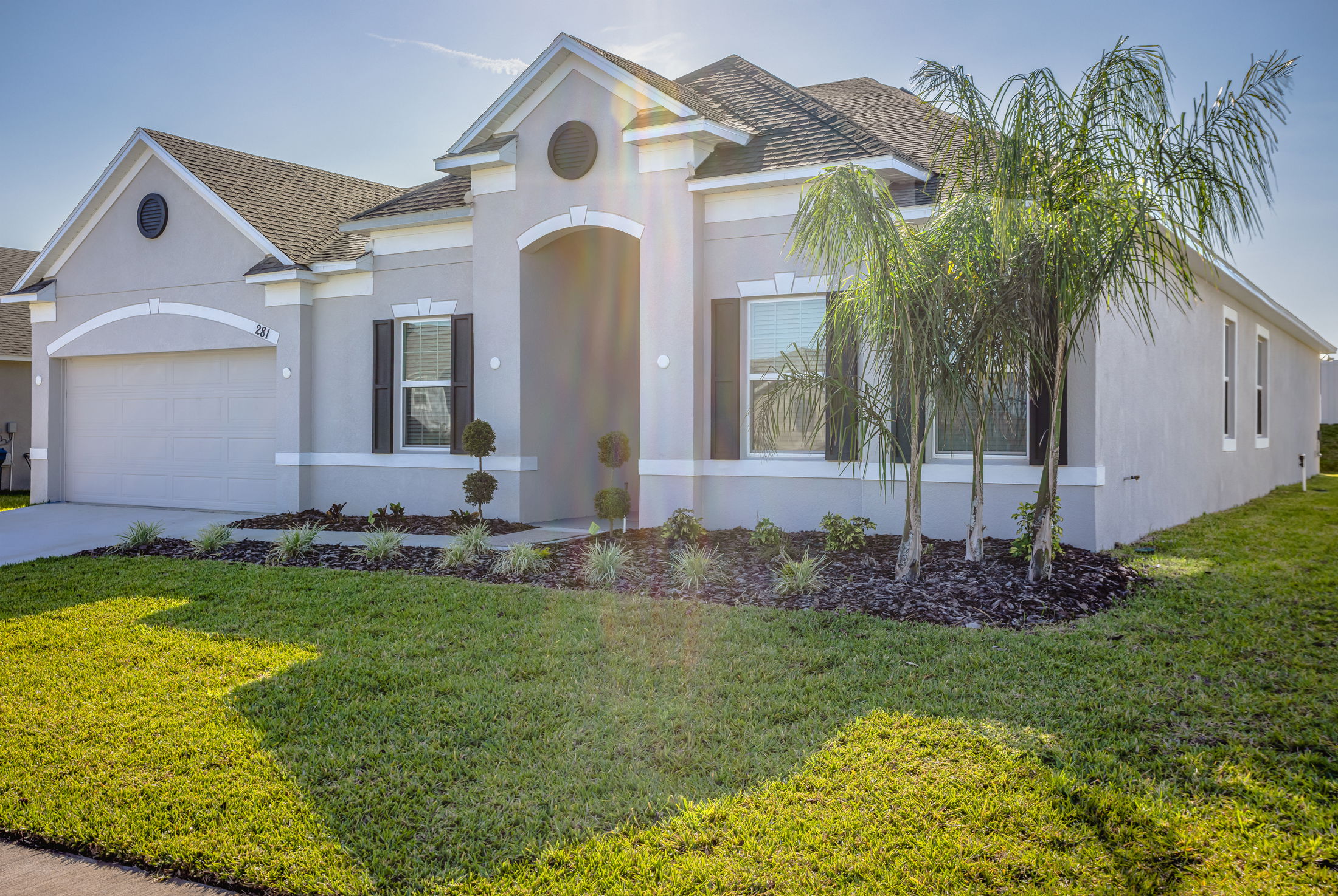 Modern single-story white house with manicured lawn and palm tree landscaping under a clear blue sky.