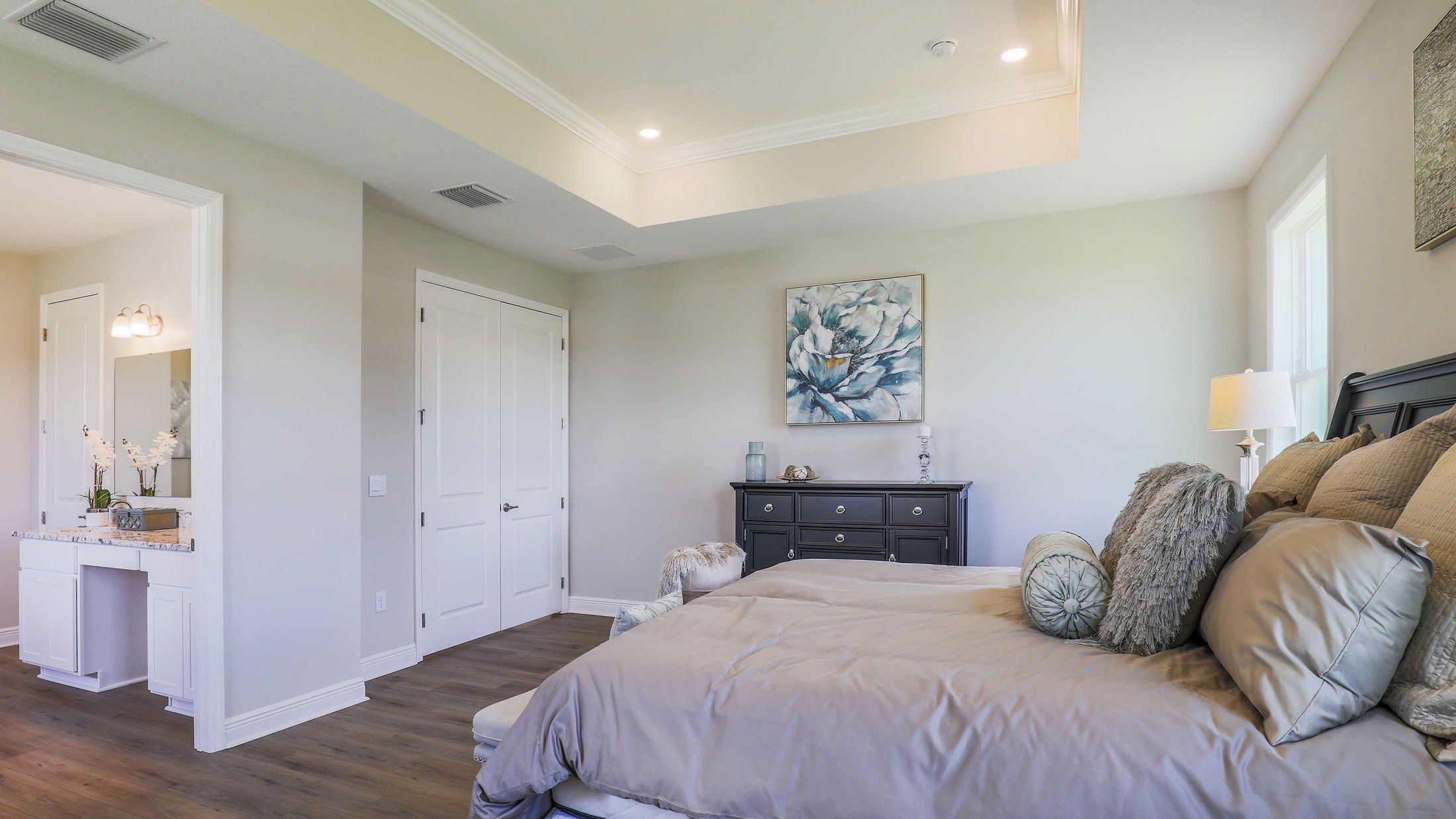 Modern bedroom with elegant gray bedding, stylish decor, and a large floral painting above a black dresser.