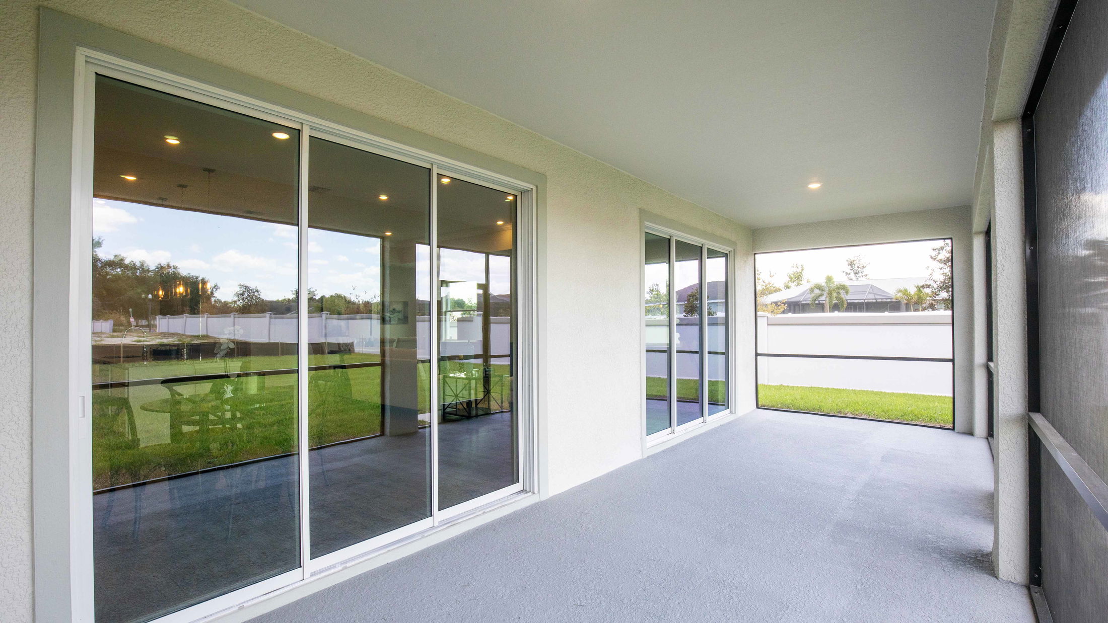 Covered patio with large sliding glass doors and a view of a fenced backyard and greenery.