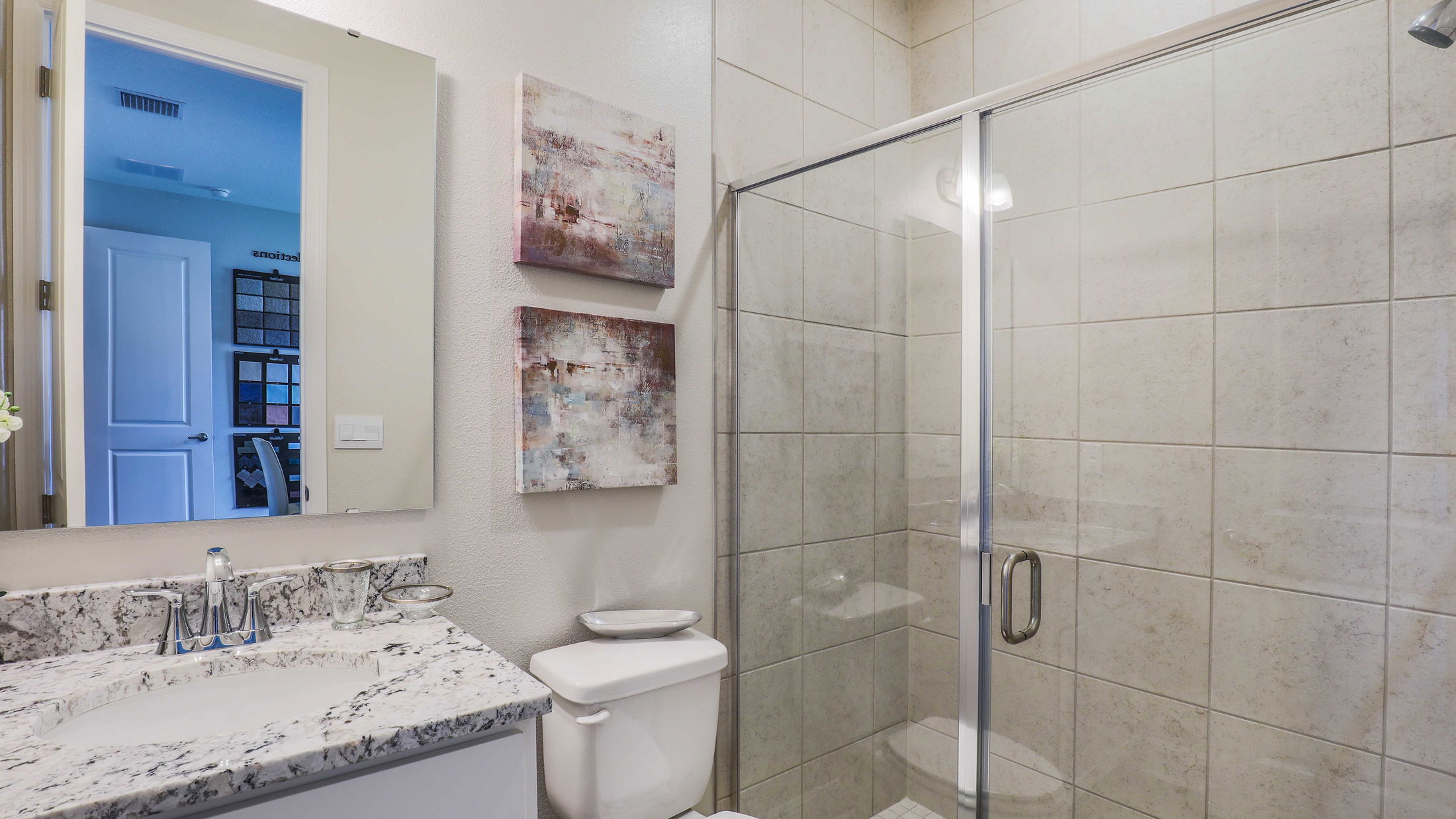 Modern bathroom with marble countertop, glass shower enclosure, and abstract wall art.