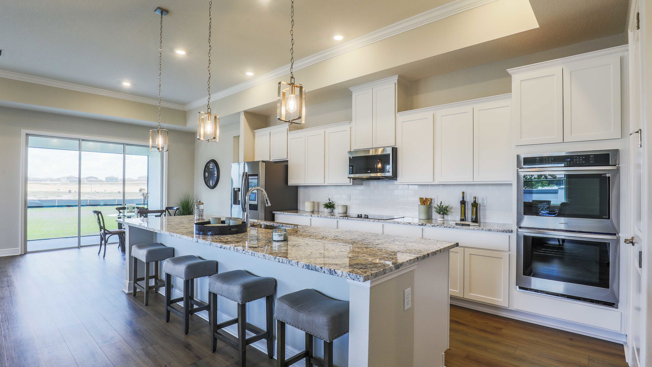 Modern kitchen with white cabinetry, granite countertops, stainless steel appliances, and pendant lighting overlooking a spacious layout with a large window.