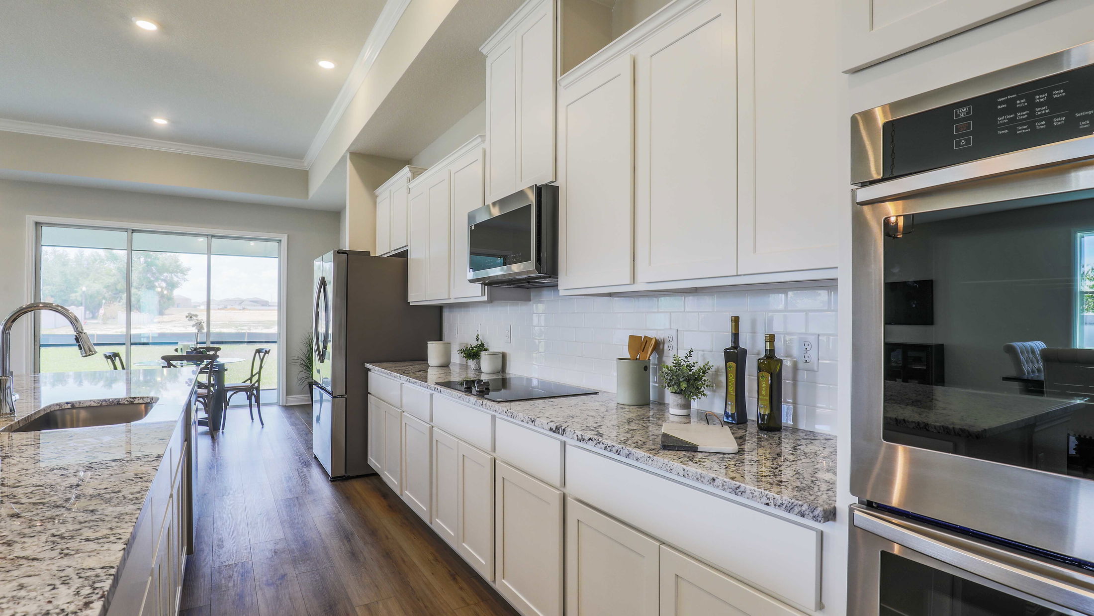 Modern kitchen with stainless steel appliances, white cabinets, granite countertops, and wooden flooring.