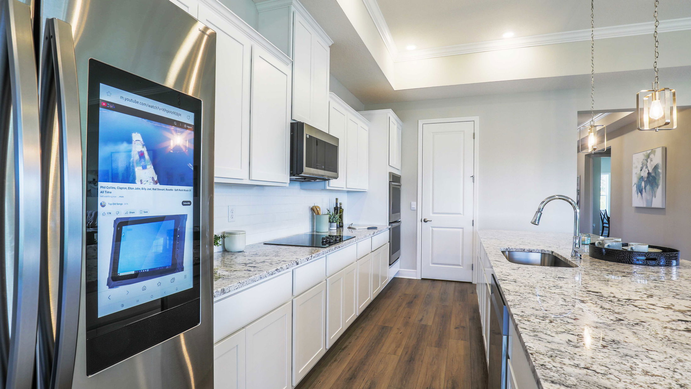 Modern kitchen with white cabinetry, granite countertops, and a smart refrigerator featuring a digital display.