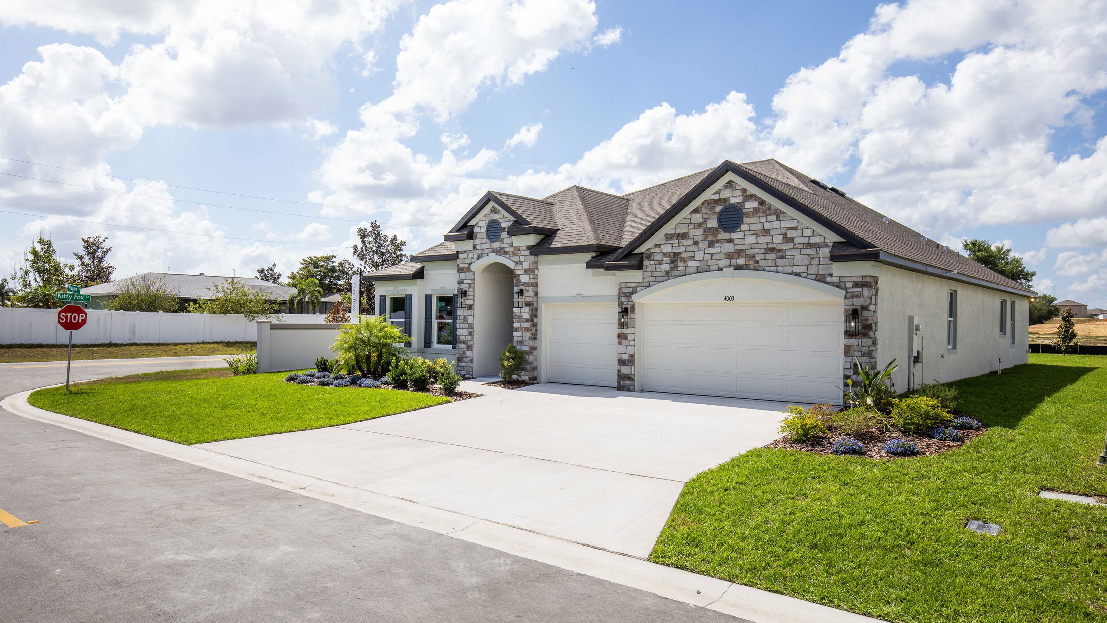 Modern suburban house with stone facade, two-car garage, and landscaped lawn on a sunny day.