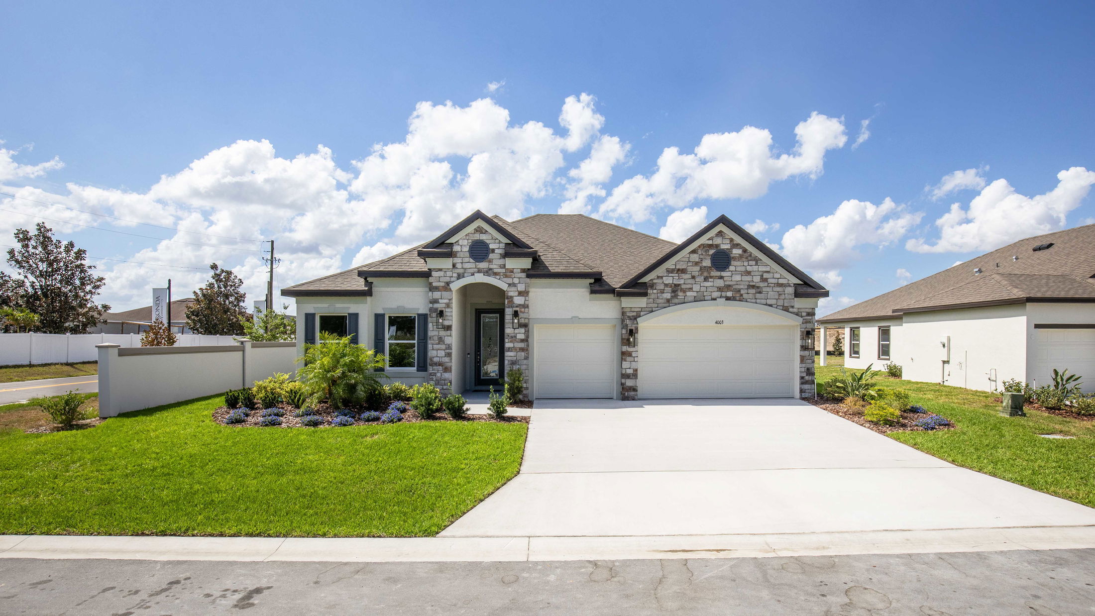Modern single-story home with stone accents, lush landscaping, and a spacious driveway under a clear blue sky.