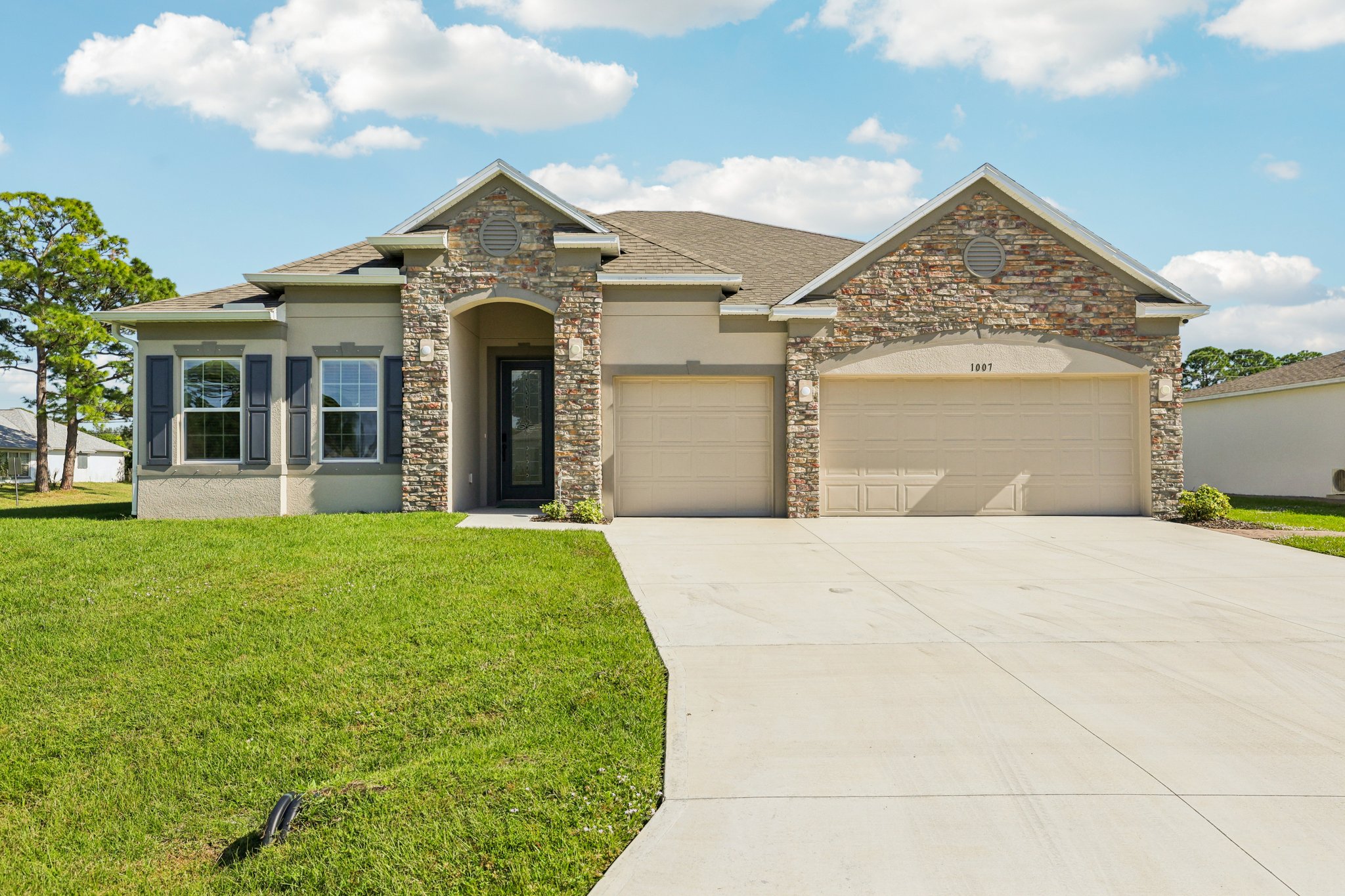 Modern single-story home with stone accents, two-car garage, and manicured lawn against a blue sky.