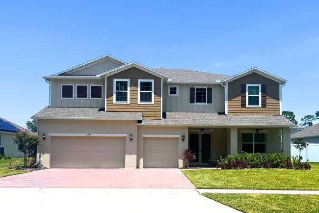 Two-story modern suburban home with three-car garage, landscaped yard, and blue sky in the background.