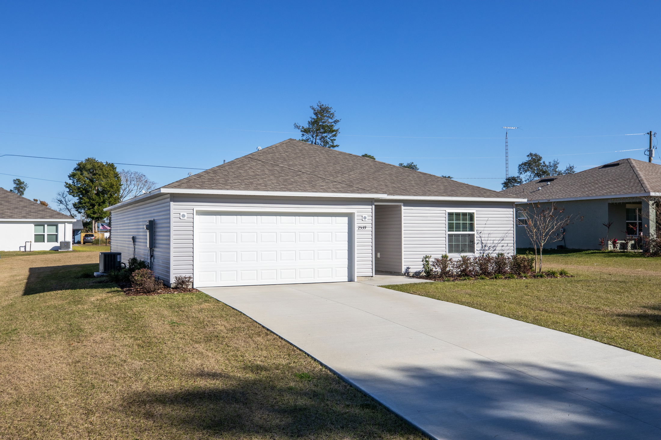Single-story suburban home with a two-car garage, gray siding, and a neatly maintained lawn on a sunny day.