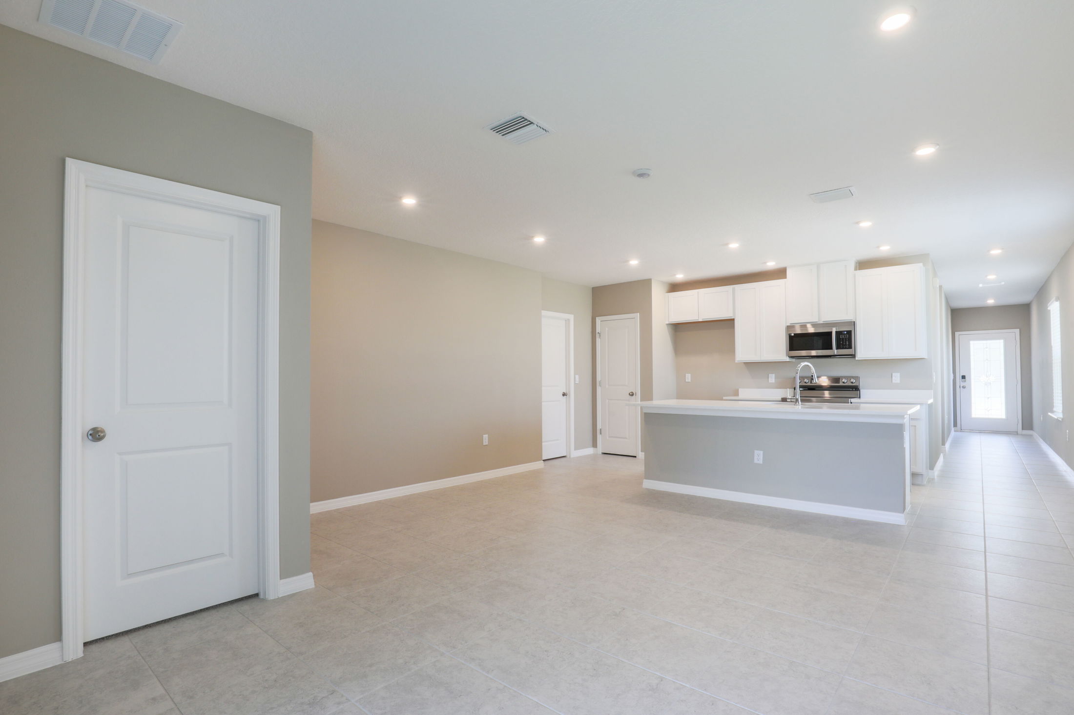 Modern open-concept kitchen with white cabinets, stainless steel appliances, and recessed lighting in a spacious, minimalist home interior.