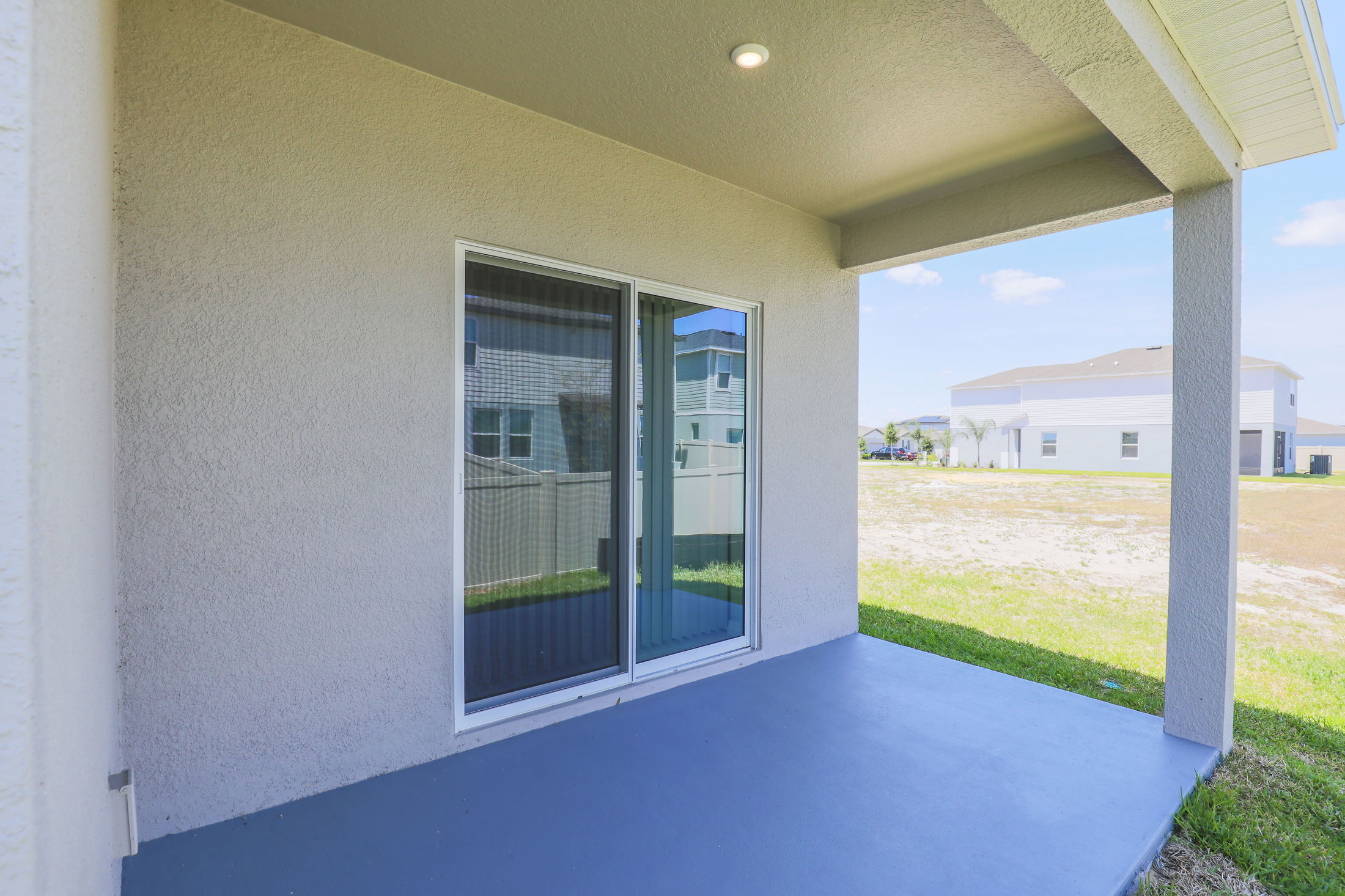 Covered patio with sliding glass doors and view of grassy backyard in suburban neighborhood.