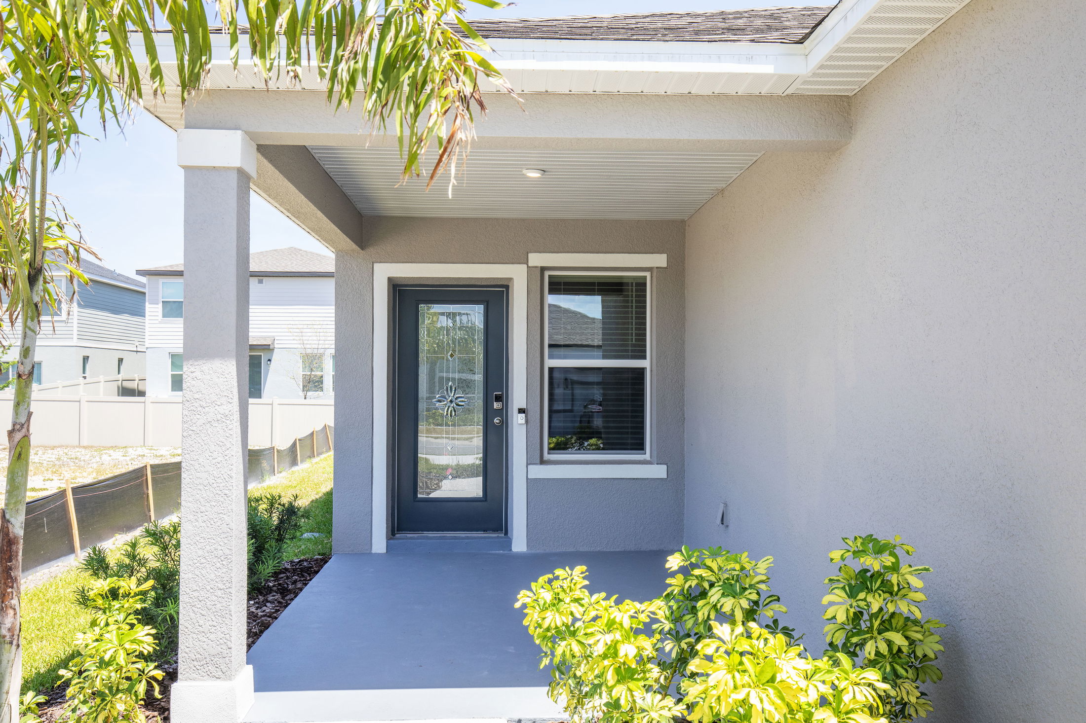 Modern home entrance with glass front door, covered porch, and green landscaping.