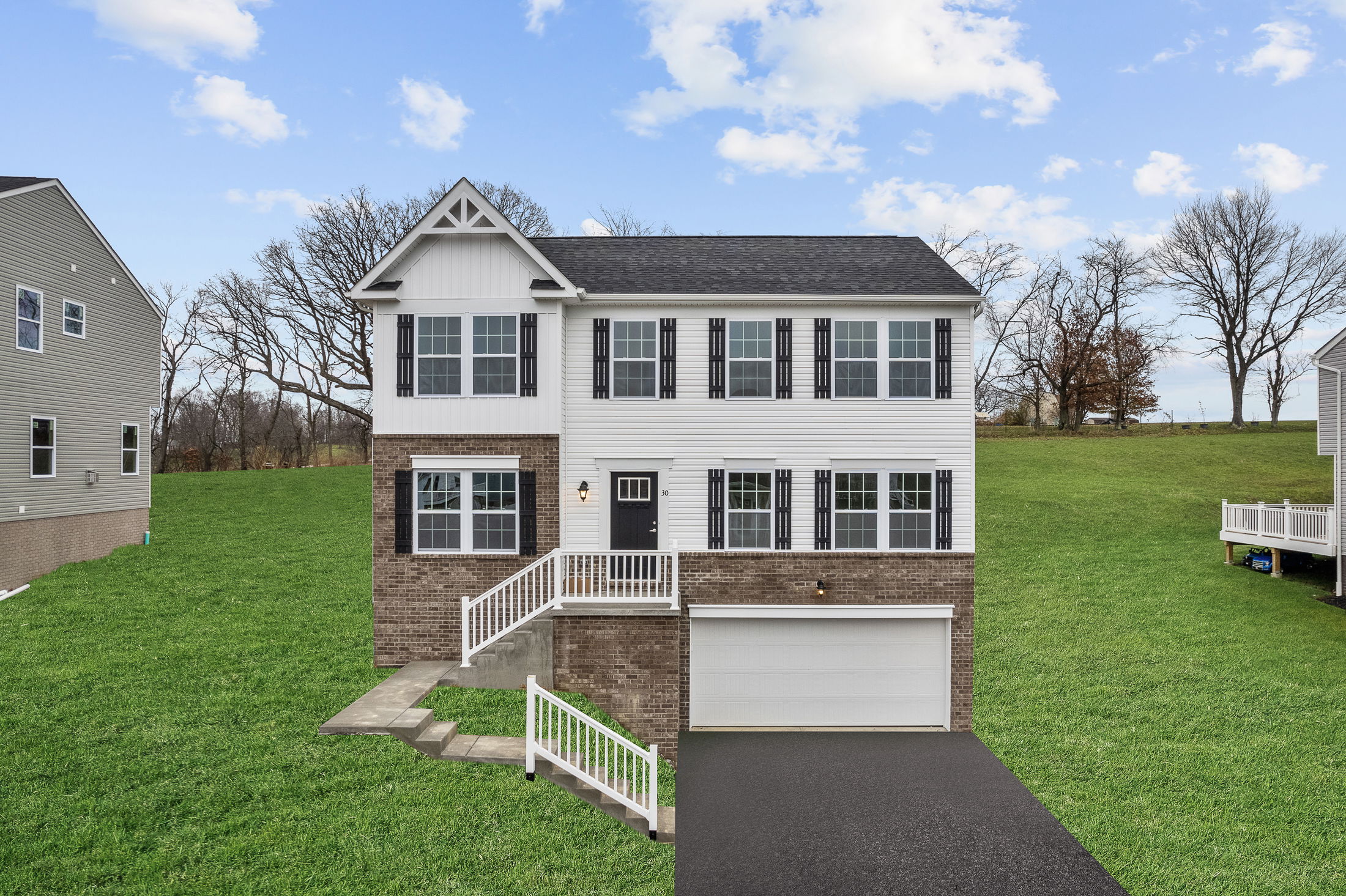 A modern two-story house with white siding, brick facade, and a spacious lawn under a clear blue sky.