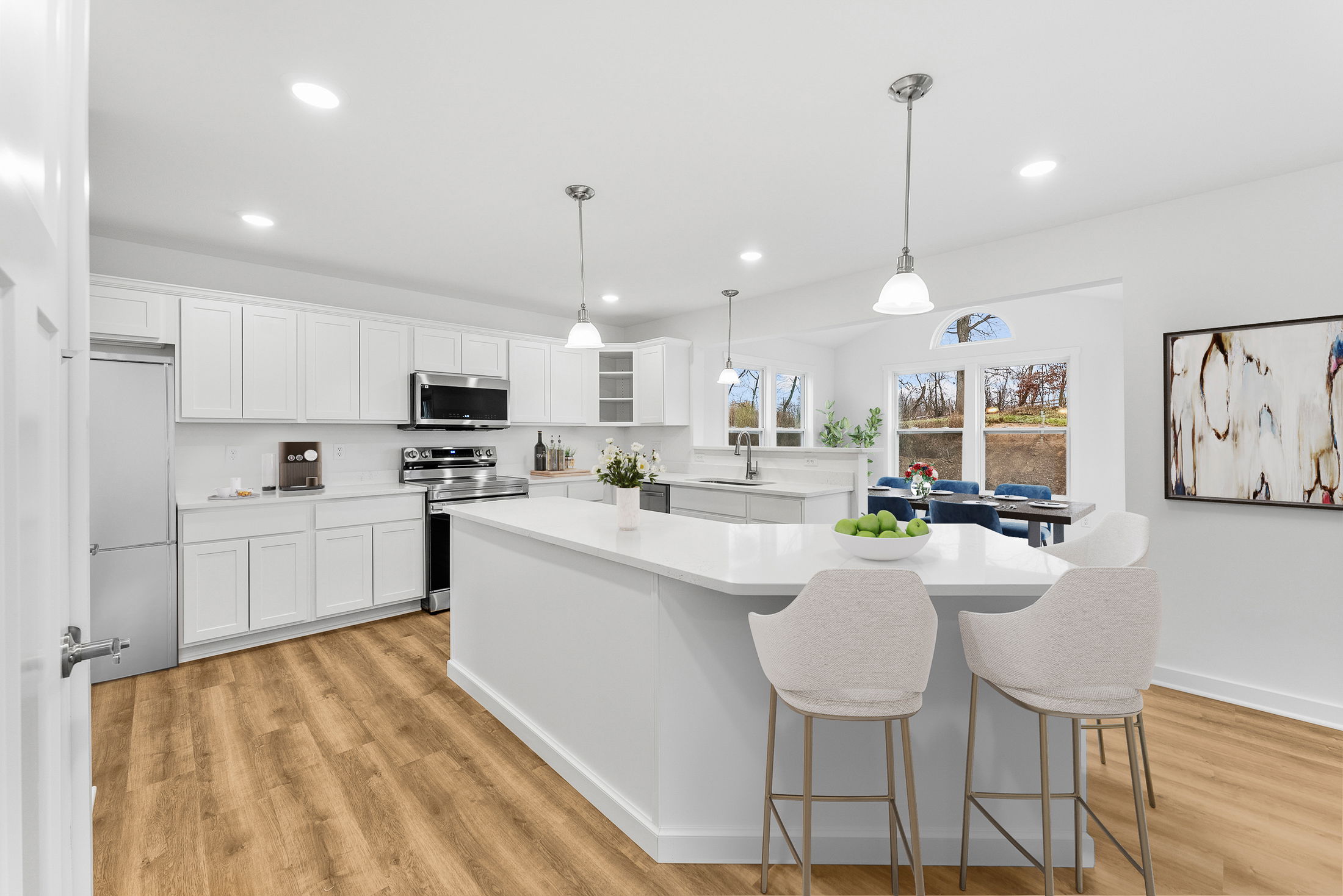 Modern kitchen interior with white cabinets, stainless steel appliances, wooden flooring, large island, and ample natural light.