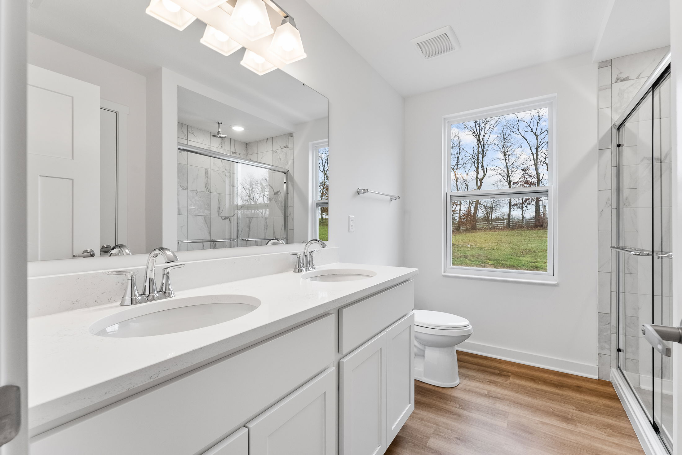 Modern bathroom with double sinks, large mirror, and a scenic window view.
