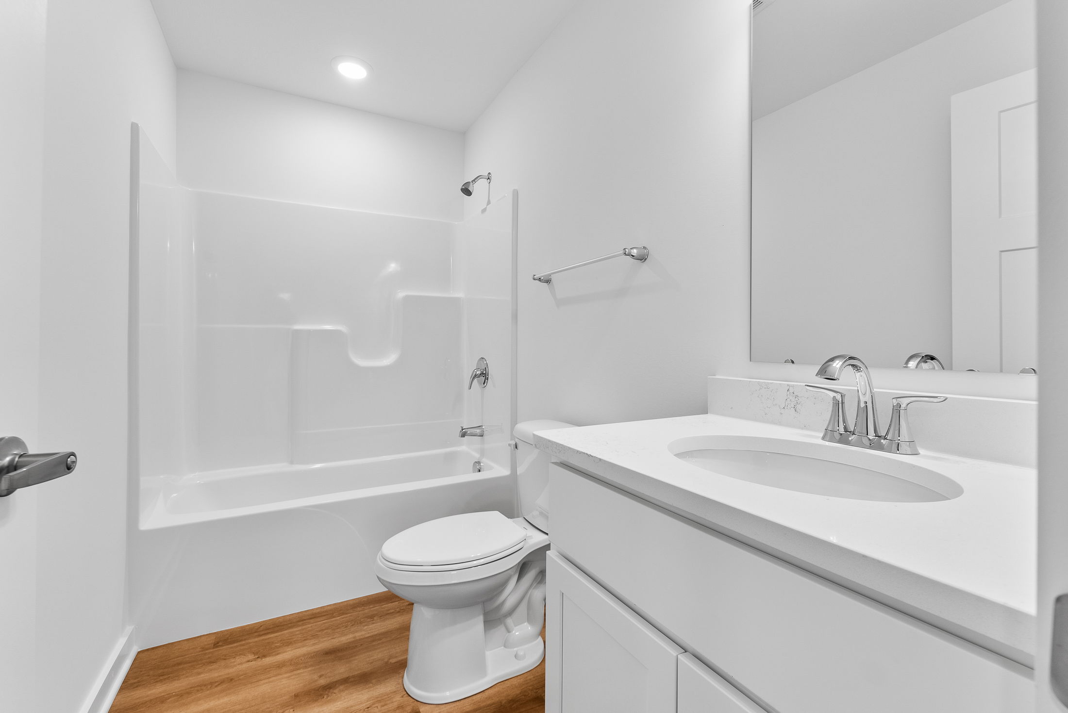 Modern white bathroom with tub-shower combo, toilet, and vanity with chrome fixtures on wood flooring.