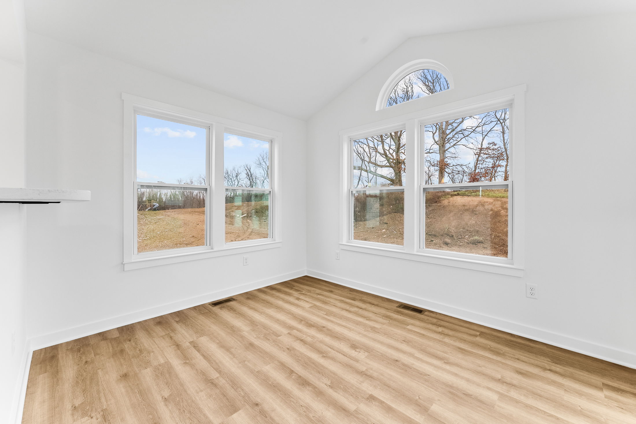 Bright, empty room with large windows, white walls, and light wood flooring overlooking a scenic outdoor landscape.