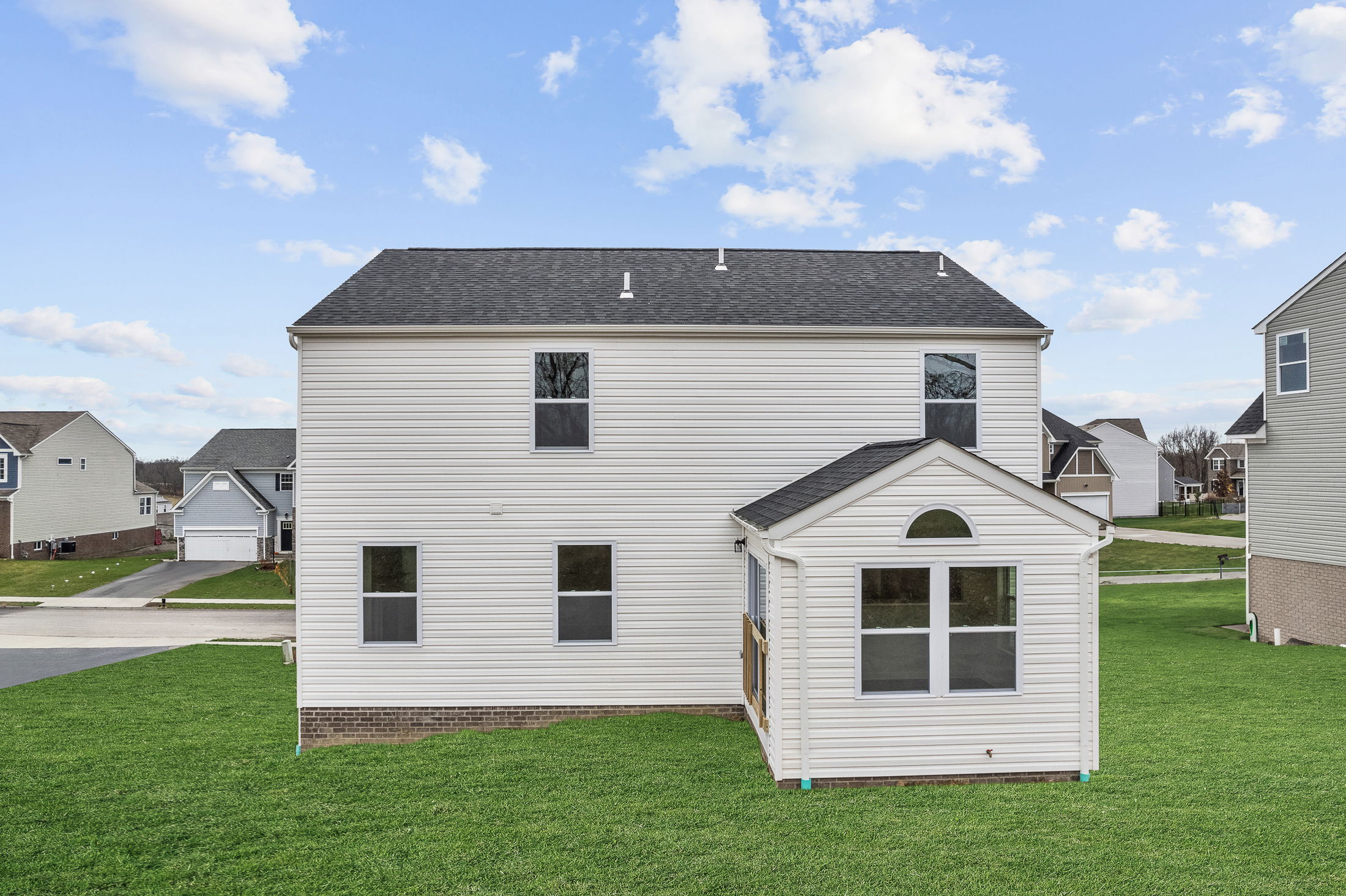 Two-story white vinyl house with an attached sunroom, surrounded by a green lawn in a suburban neighborhood.