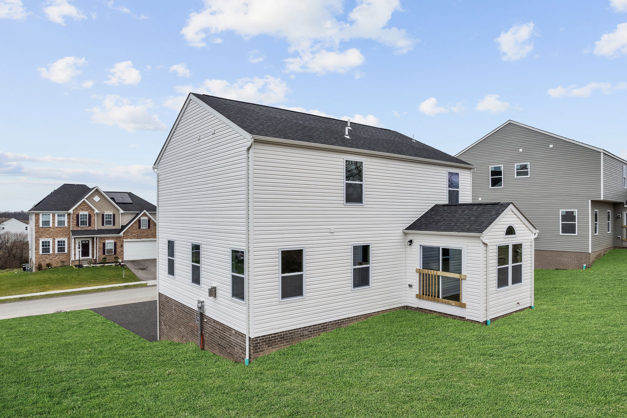 Modern two-story suburban house with a brick foundation and vinyl siding, set in a residential neighborhood under a blue sky.