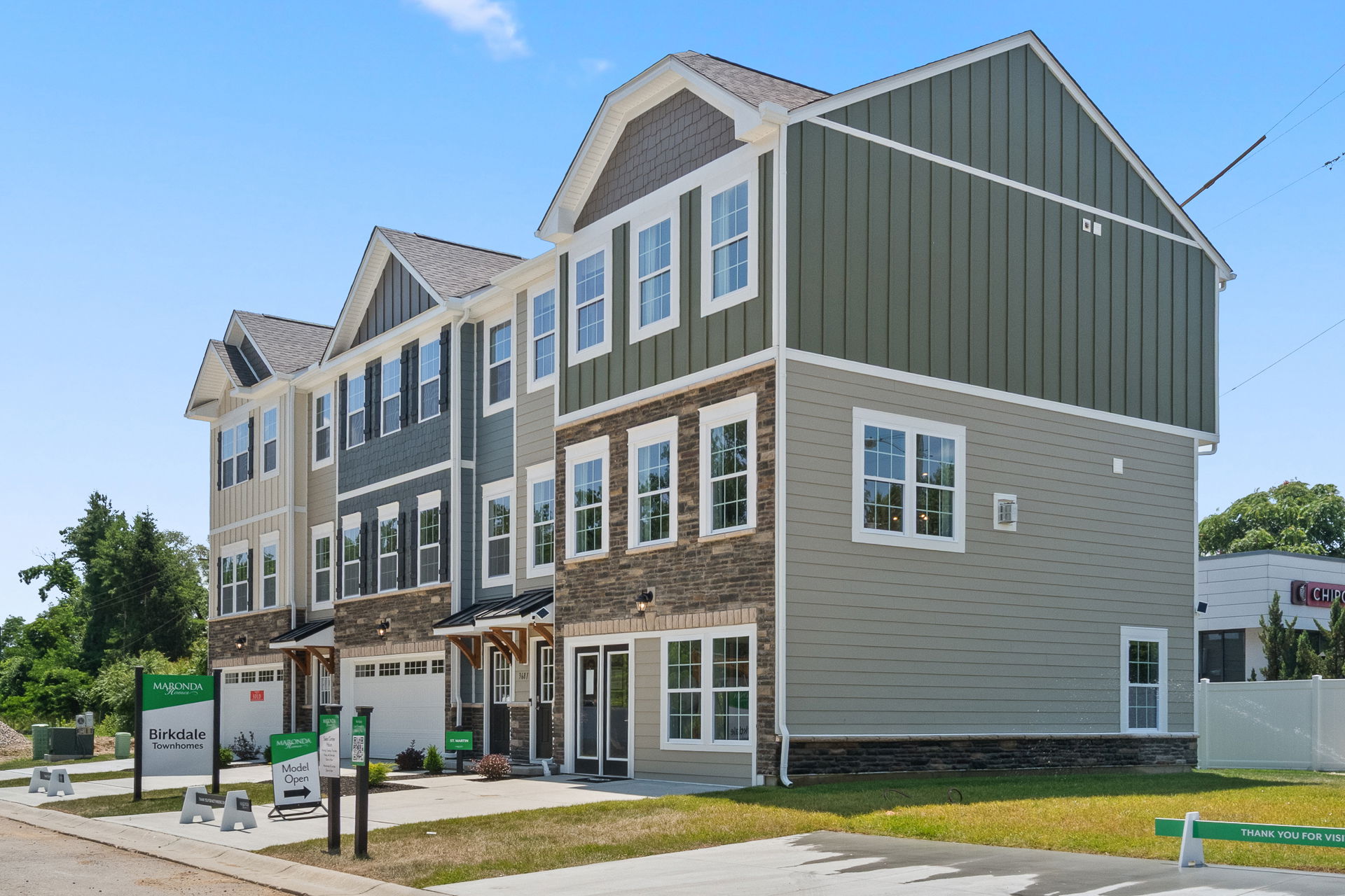 Exterior view of a modern new-build, three-story townhouse with green and beige siding, located in a residential neighborhood.