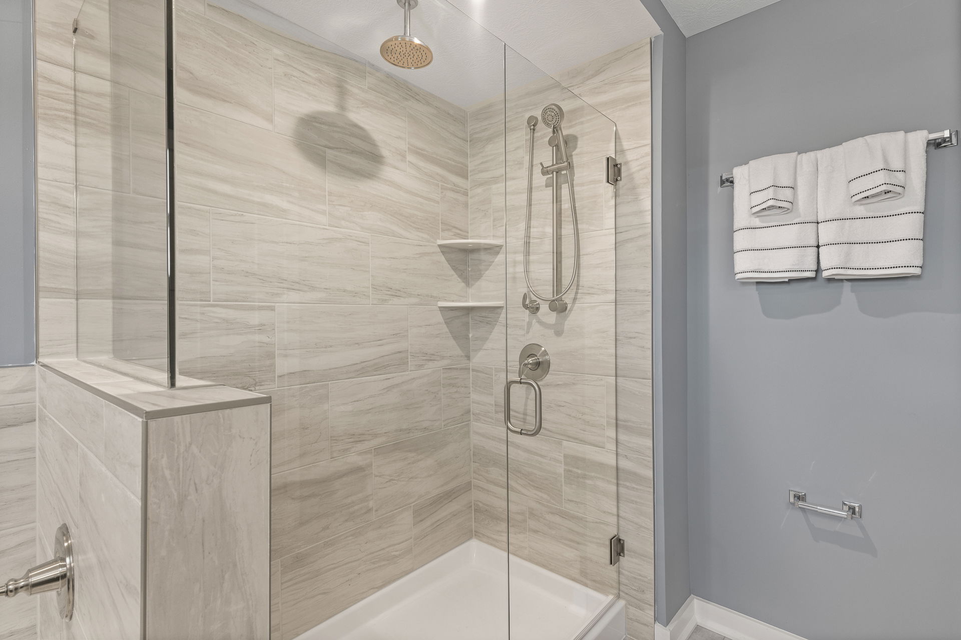 Modern bathroom with a glass-enclosed shower, beige tile walls, and stainless steel fixtures.