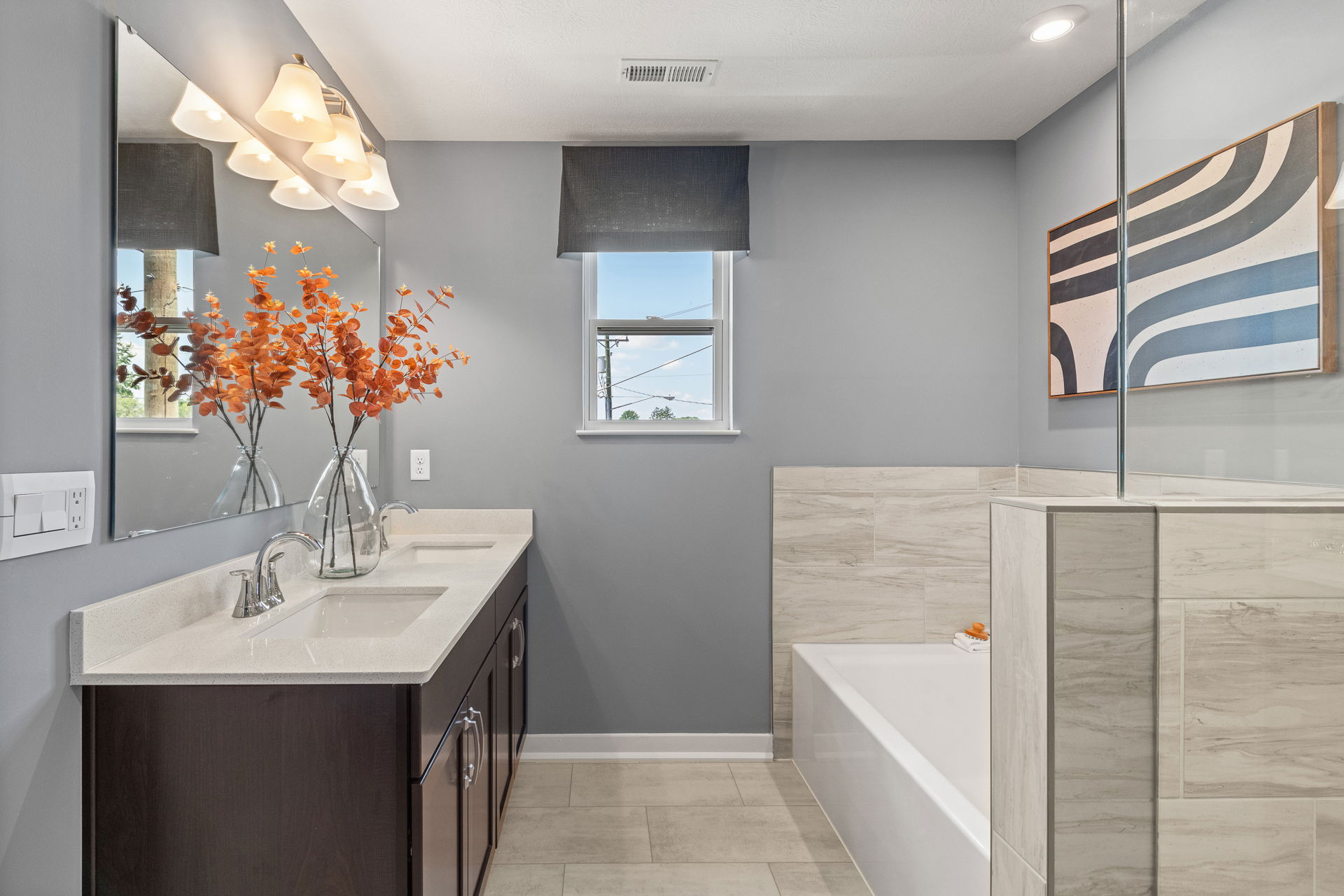 Modern bathroom with dual sinks, a glass shower, and decorative orange foliage in a vase.
