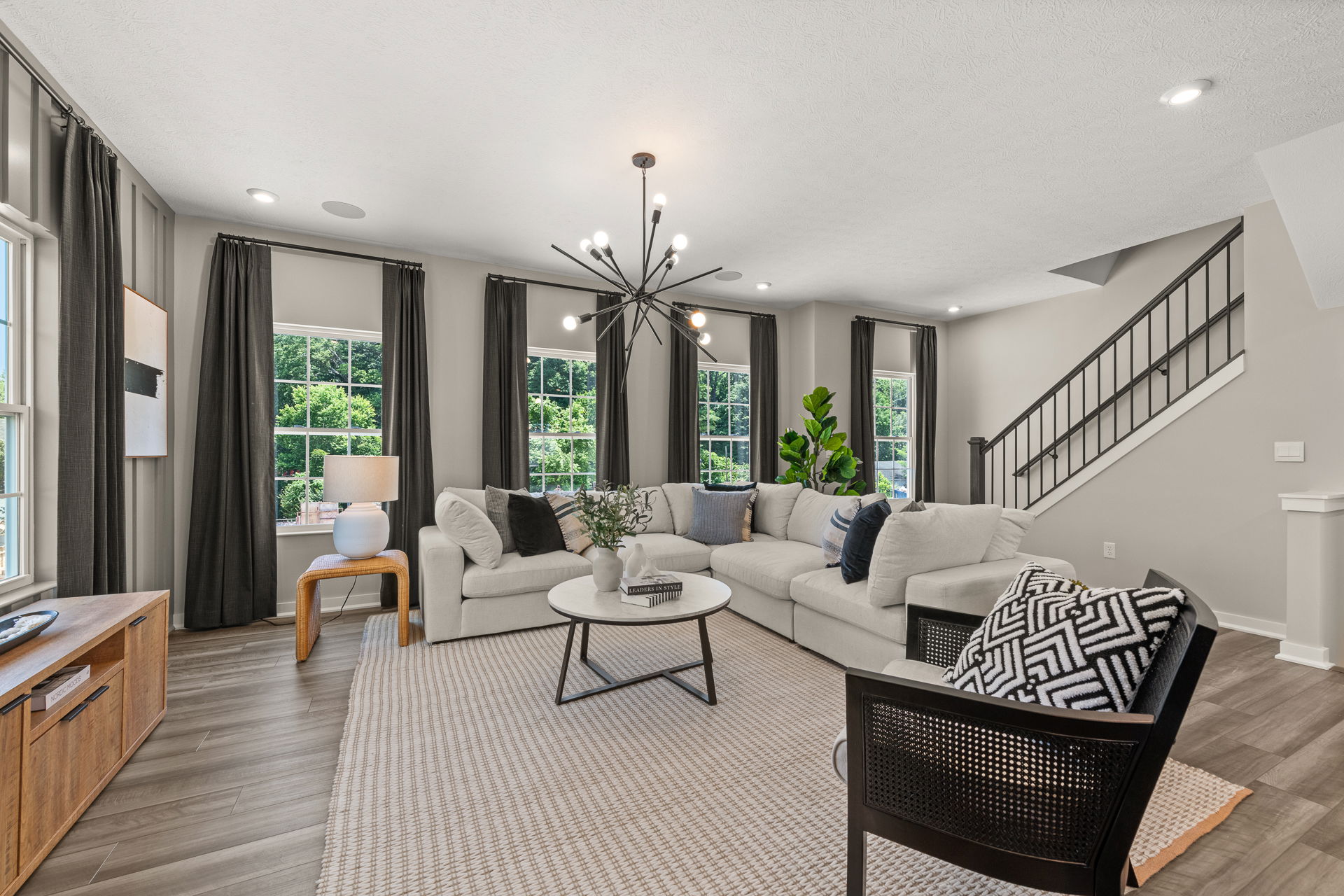Modern living room with a gray sectional sofa, contemporary chandelier, large windows with dark curtains, and a stylish area rug.