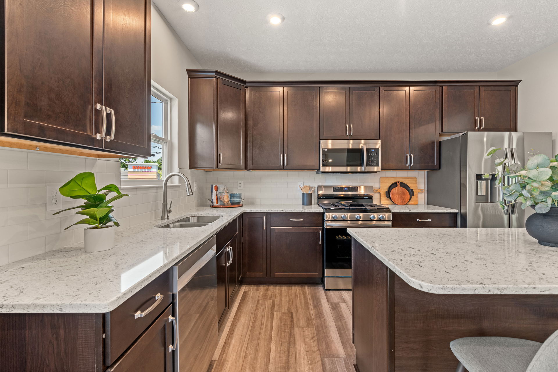 Modern kitchen with dark wood cabinets, marble countertops, stainless steel appliances, and decorative plants.