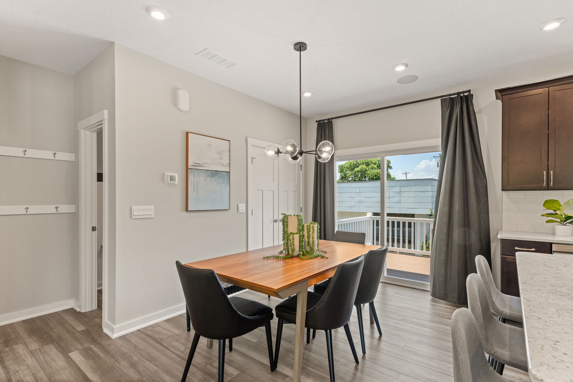 Modern dining room with a wooden table, black chairs, contemporary chandelier, and sliding glass doors leading to a deck.