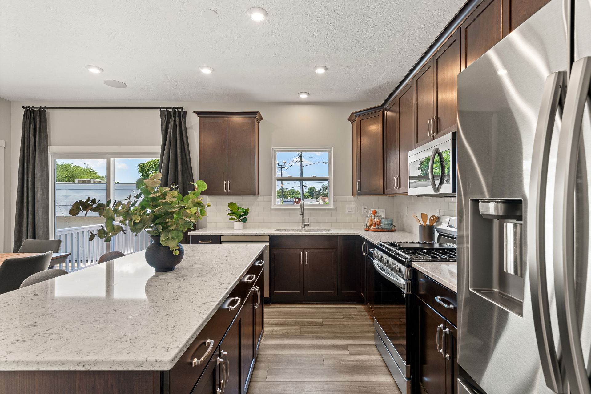 Modern kitchen with dark cabinetry, stainless steel appliances, and a large marble island countertop adorned with a plant, offering a bright and stylish cooking space.