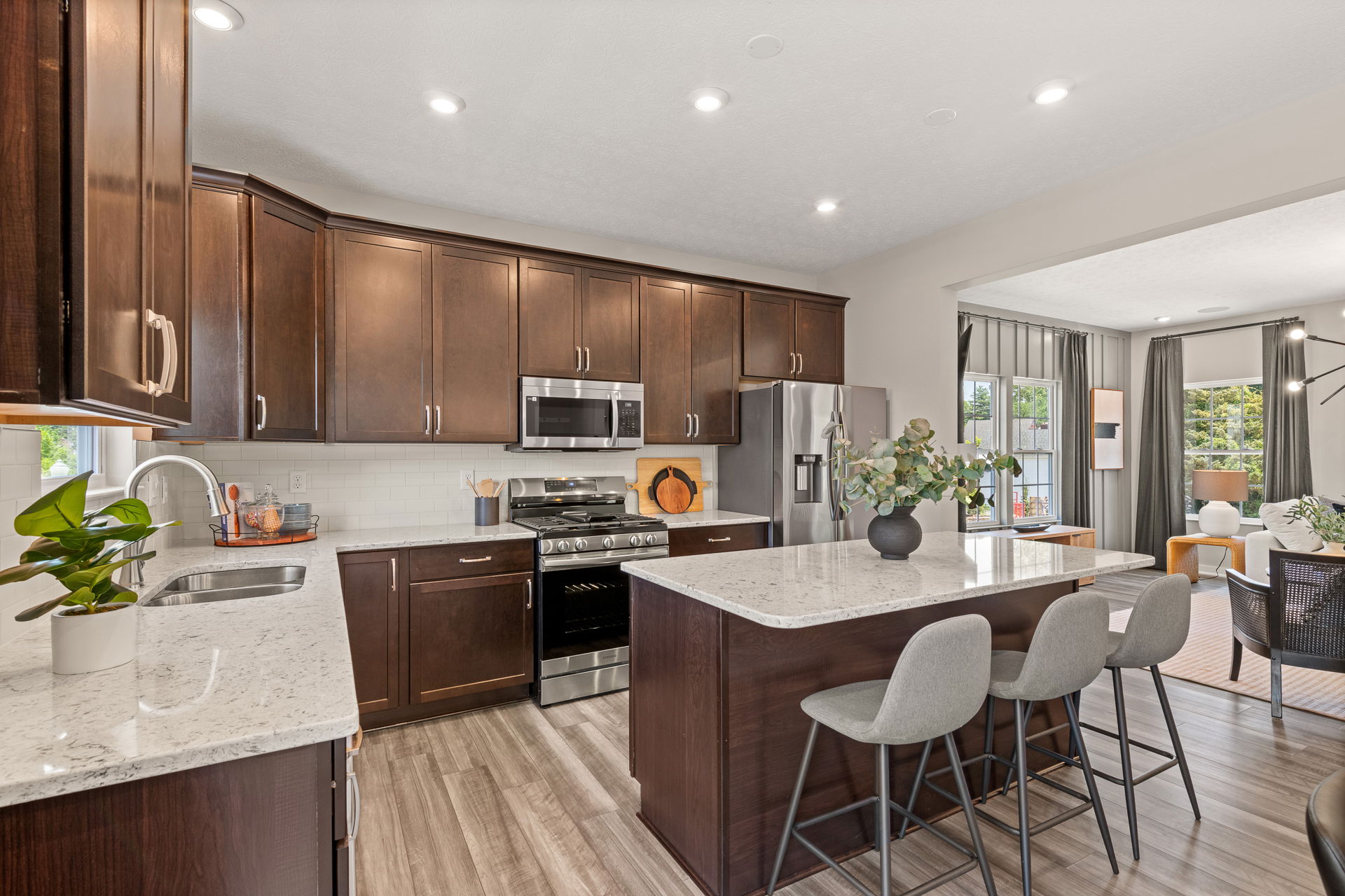 Modern kitchen with dark wood cabinets, stainless steel appliances, and a marble island with grey barstools.