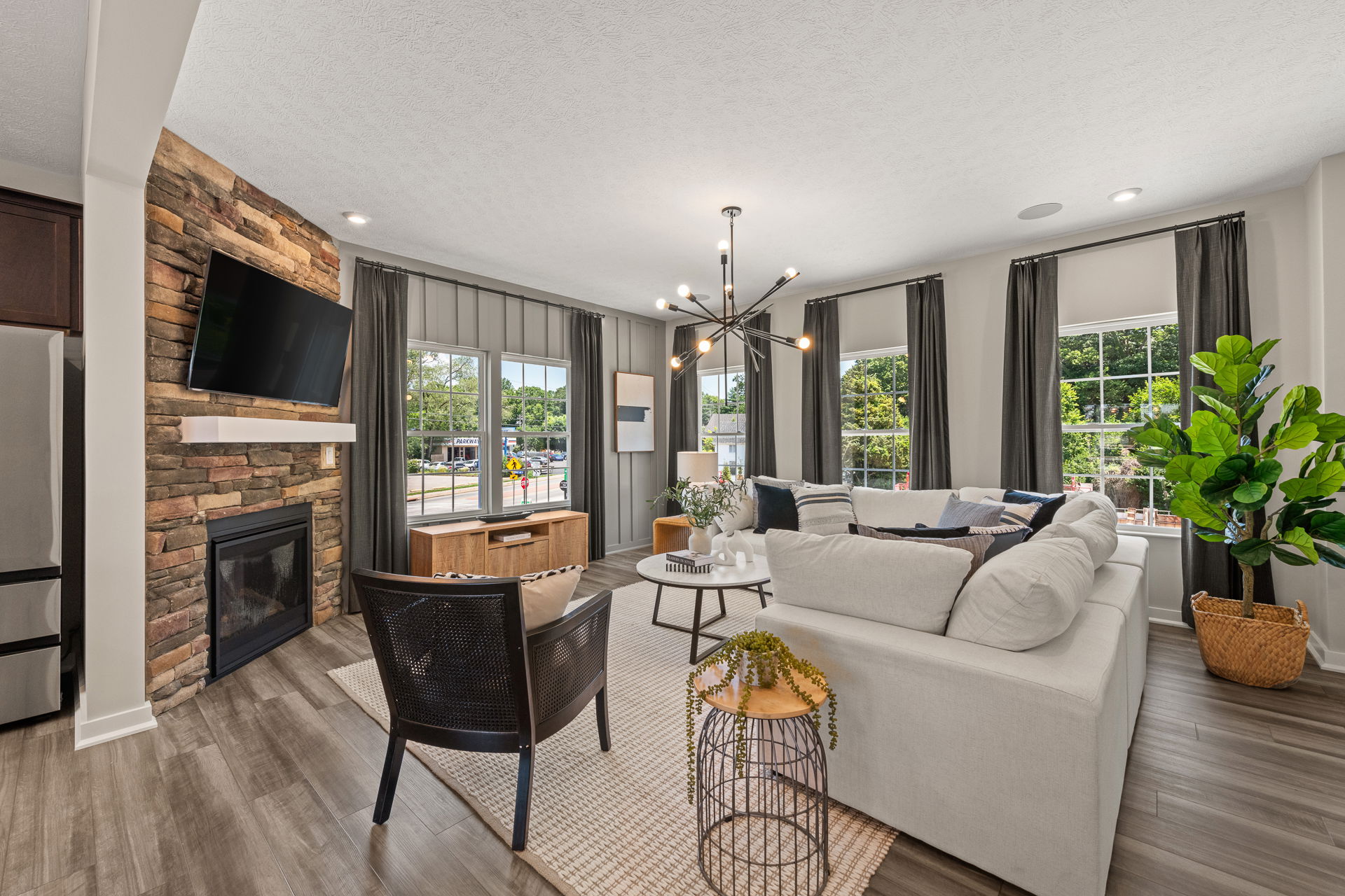 Modern living room with large windows, sectional sofa, stone fireplace, wooden floors, and chic lighting.