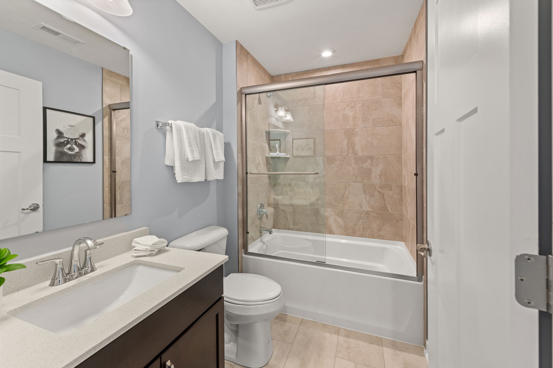 Modern bathroom with glass-enclosed bathtub, tiled walls, and a vanity with a white countertop.