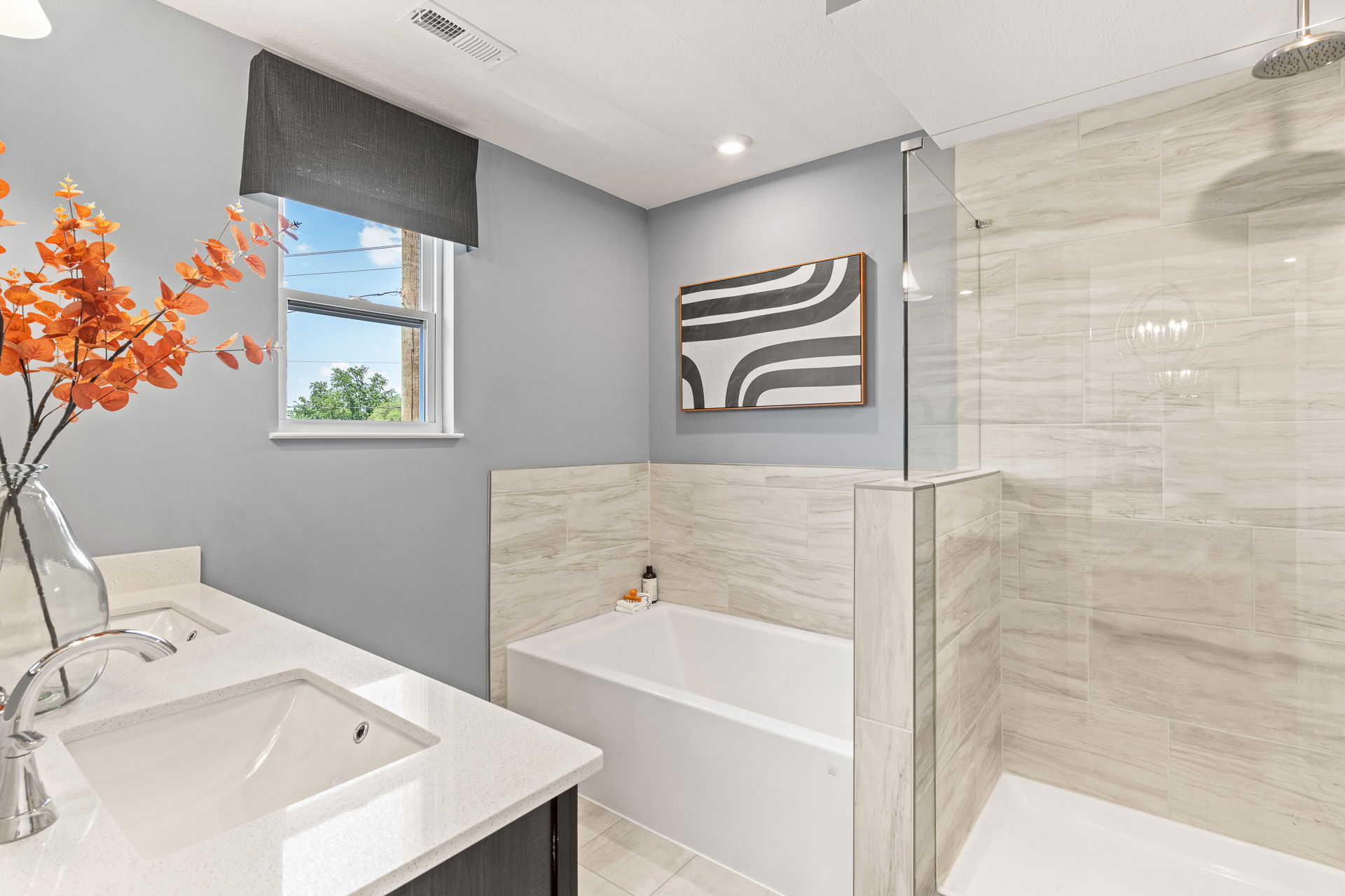 Modern bathroom with a sleek double sink vanity, orange floral decor, a rectangular bathtub, and a stylish walk-in shower with neutral tile.
