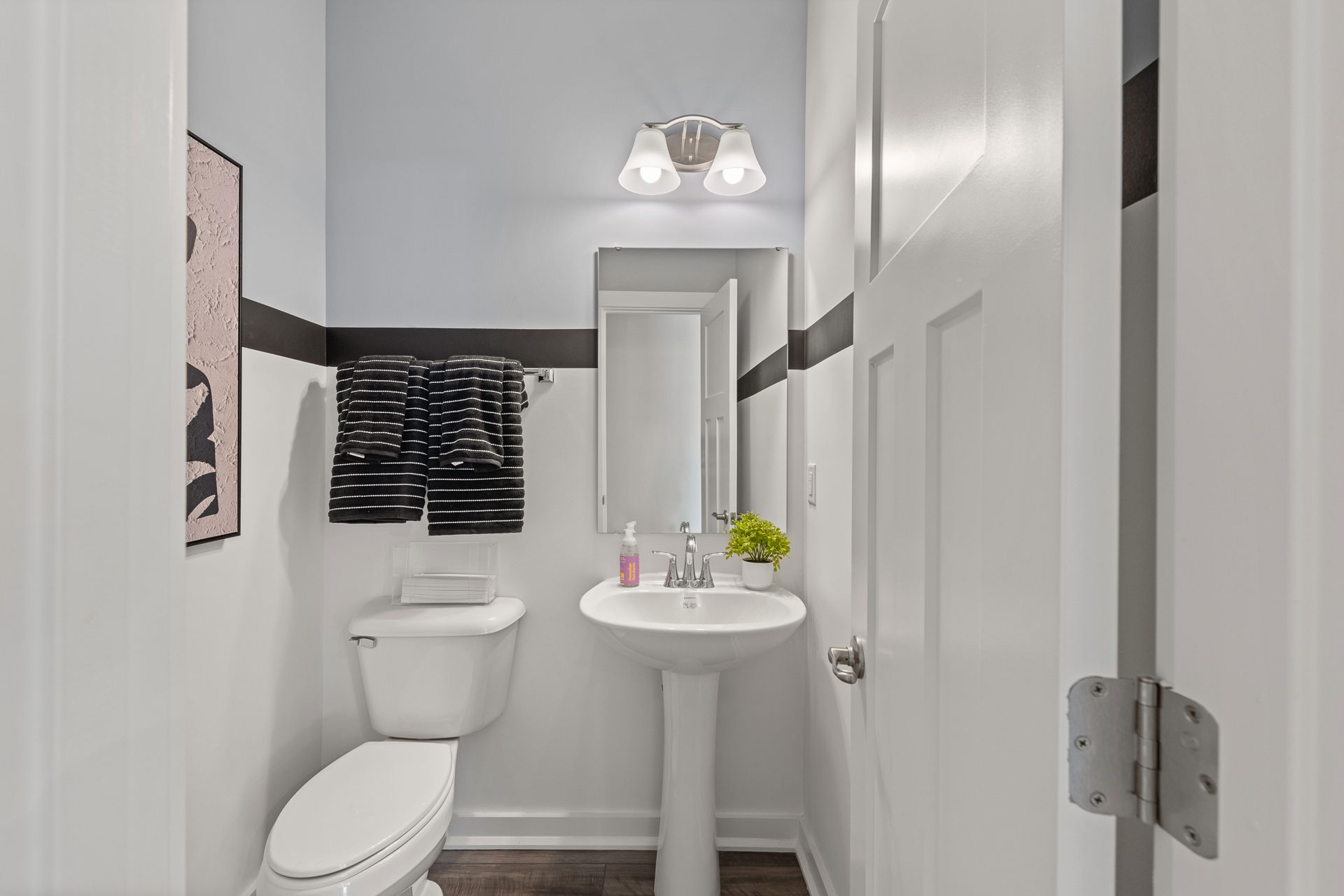 Modern small bathroom with a white pedestal sink, toilet, striped towels, and minimal decor.